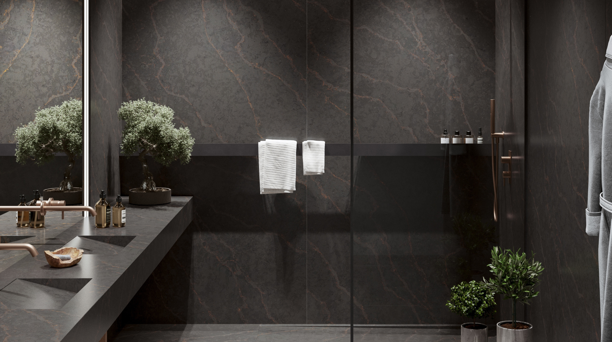 Baño moderno con paredes de mármol oscuro, un lavabo de piedra con accesorios de bronce, dos plantas decorativas y toallas blancas colgadas en un gancho.