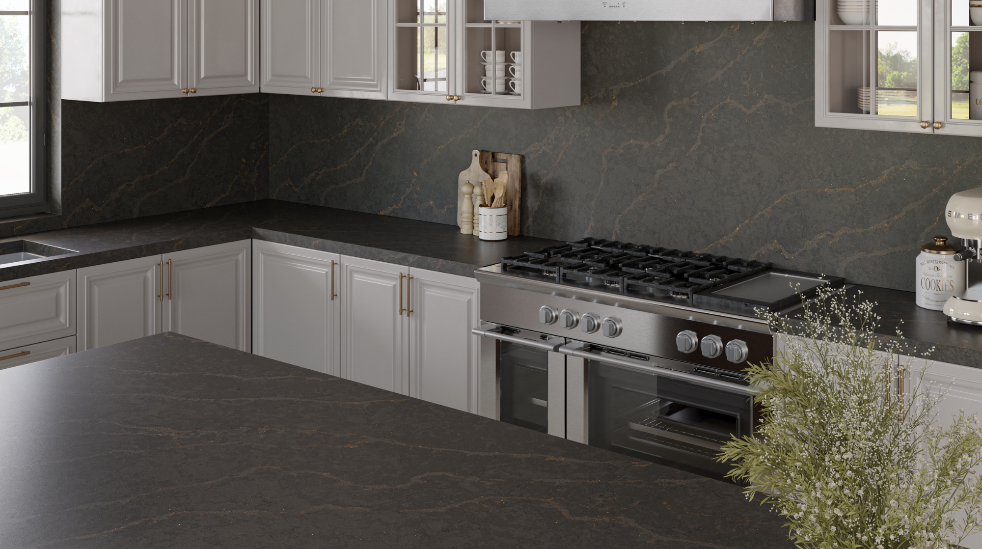 Cocina moderna con gabinetes grises y encimeras de piedra negra, estufa de acero inoxidable, y decoración con utensilios de cocina y plantas