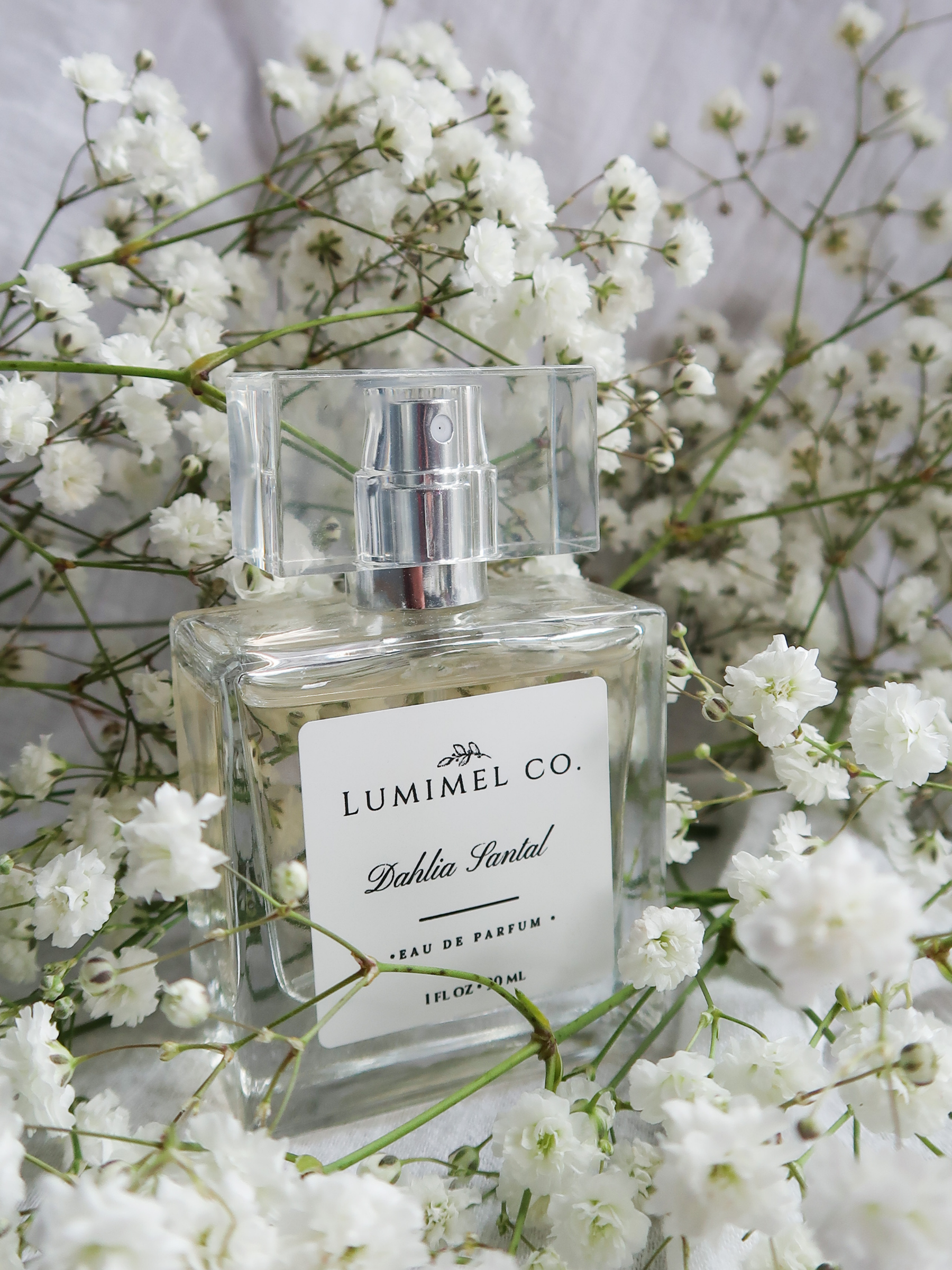 A clear glass perfume bottle with a rectangular shape, topped with a rectangular glass cap, among white baby's breath flowers.