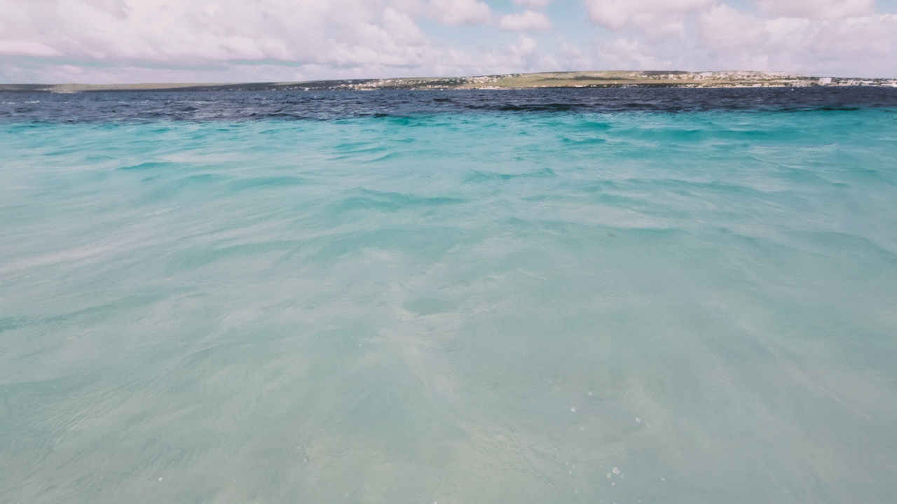 Calm turquoise ocean water with slight waves, distant landmass under a cloudy sky.