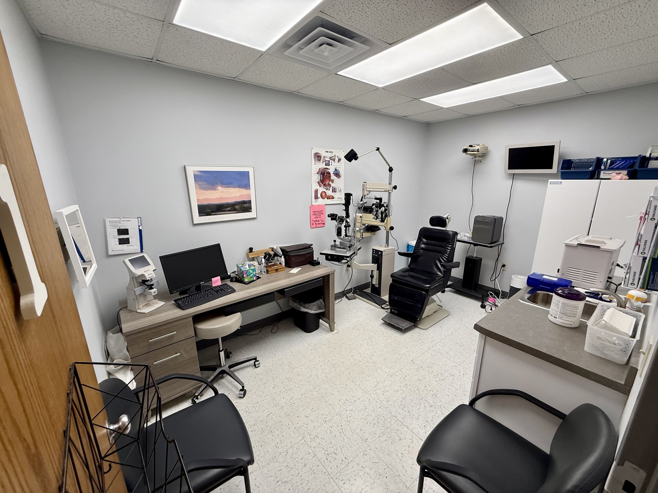 Medical examination room with eye testing equipment, computer, and chairs.