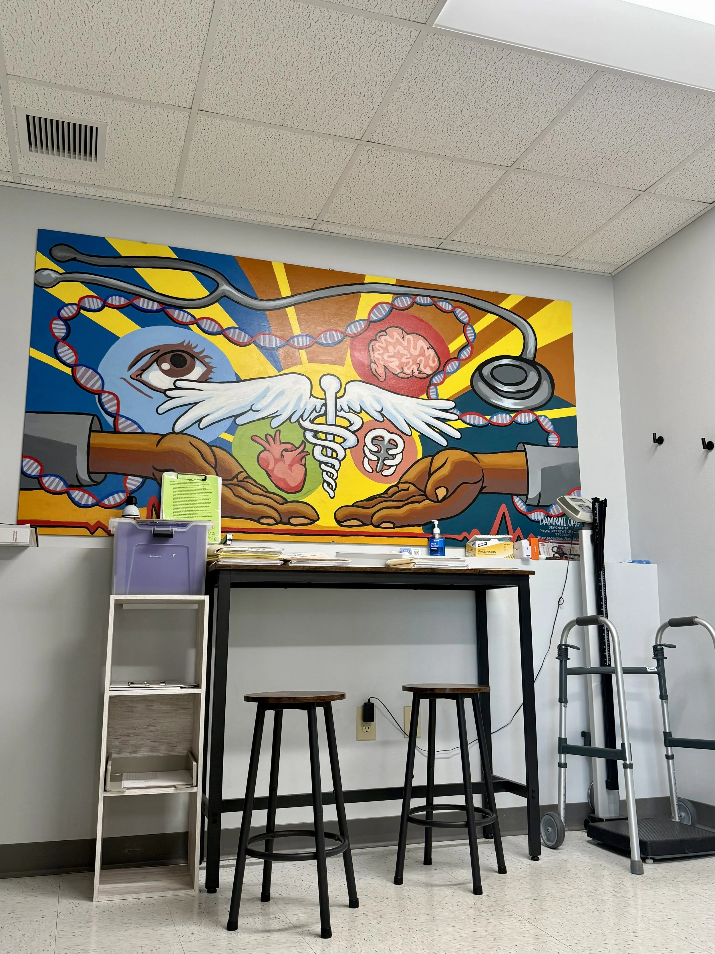 Medical office with a colorful mural on the wall depicting a large eye, brain, heart, DNA strand, wings, stethoscope, and medical symbols. There are three high black stools, a small open shelving unit, and a treadmill with crutches and medical supplies nearby.