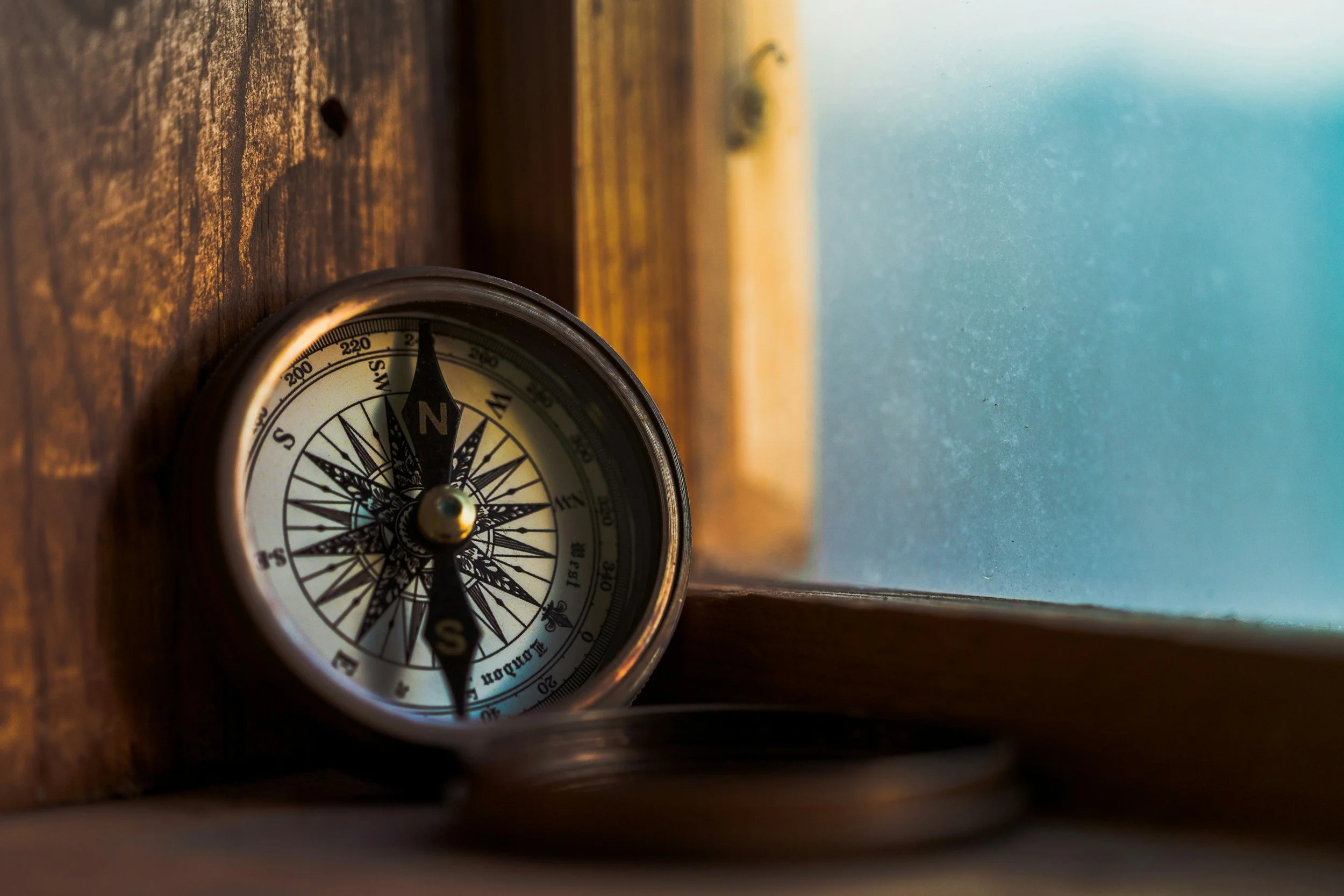 A compass leaning against a wooden surface near a window with frosted glass.