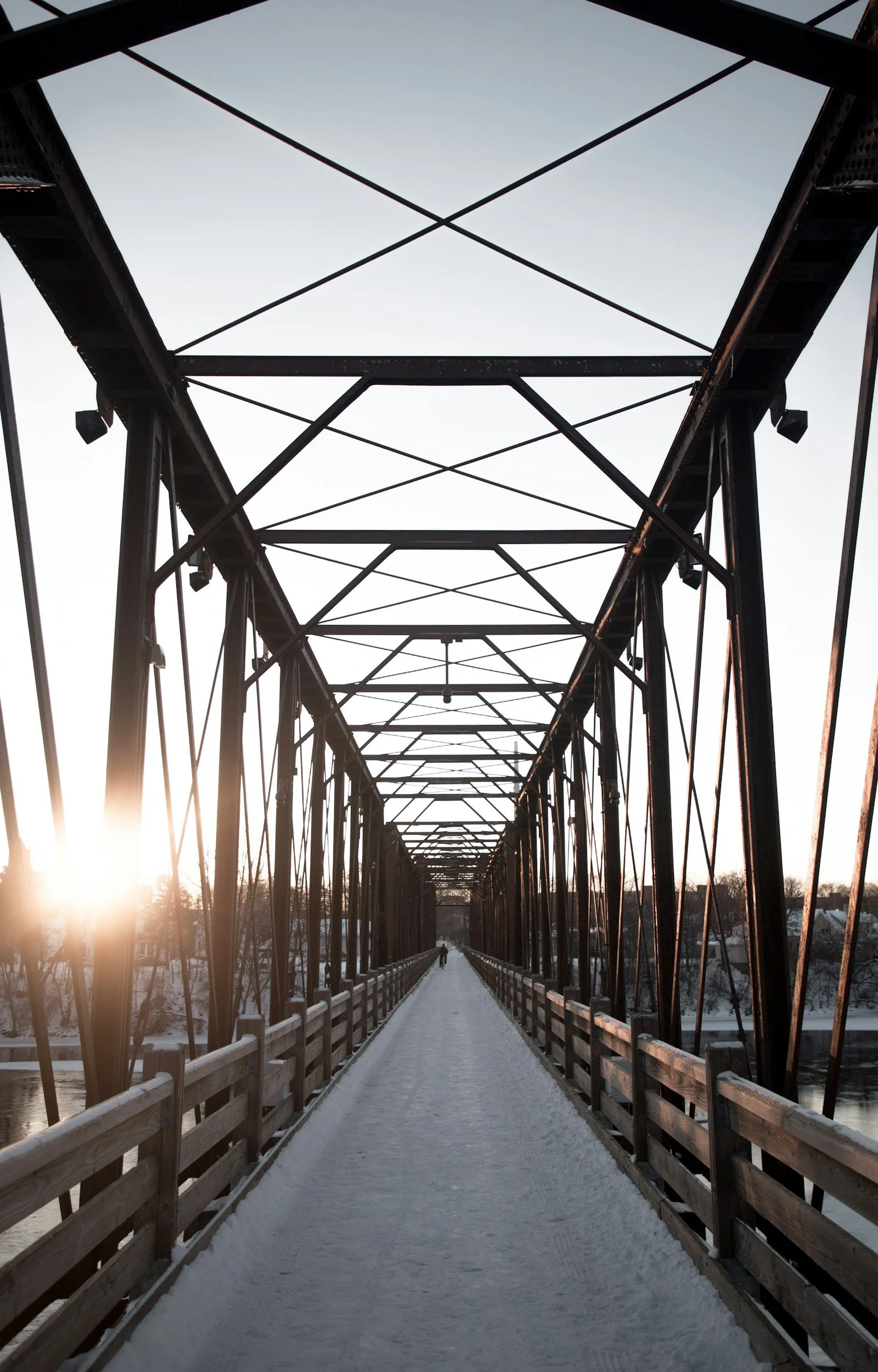 Snow-covered pedestrian bridge with metal framework at sunset, winter landscape