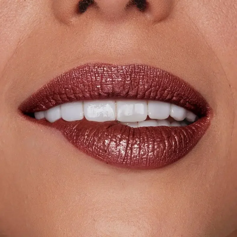 Close-up de lábios com batom metálico dourado e sorriso com dentes brancos