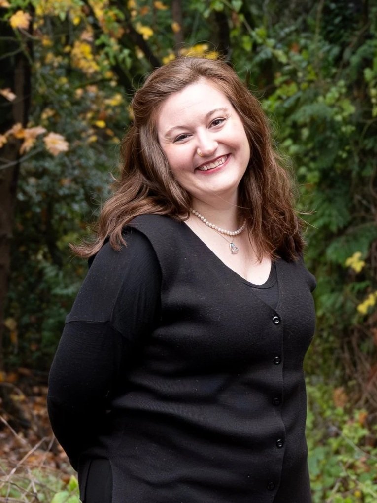 Person smiling outdoors with a background of green foliage.