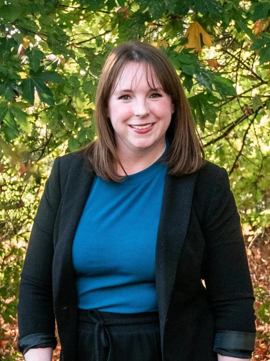 Woman smiling in a natural setting with green foliage background.