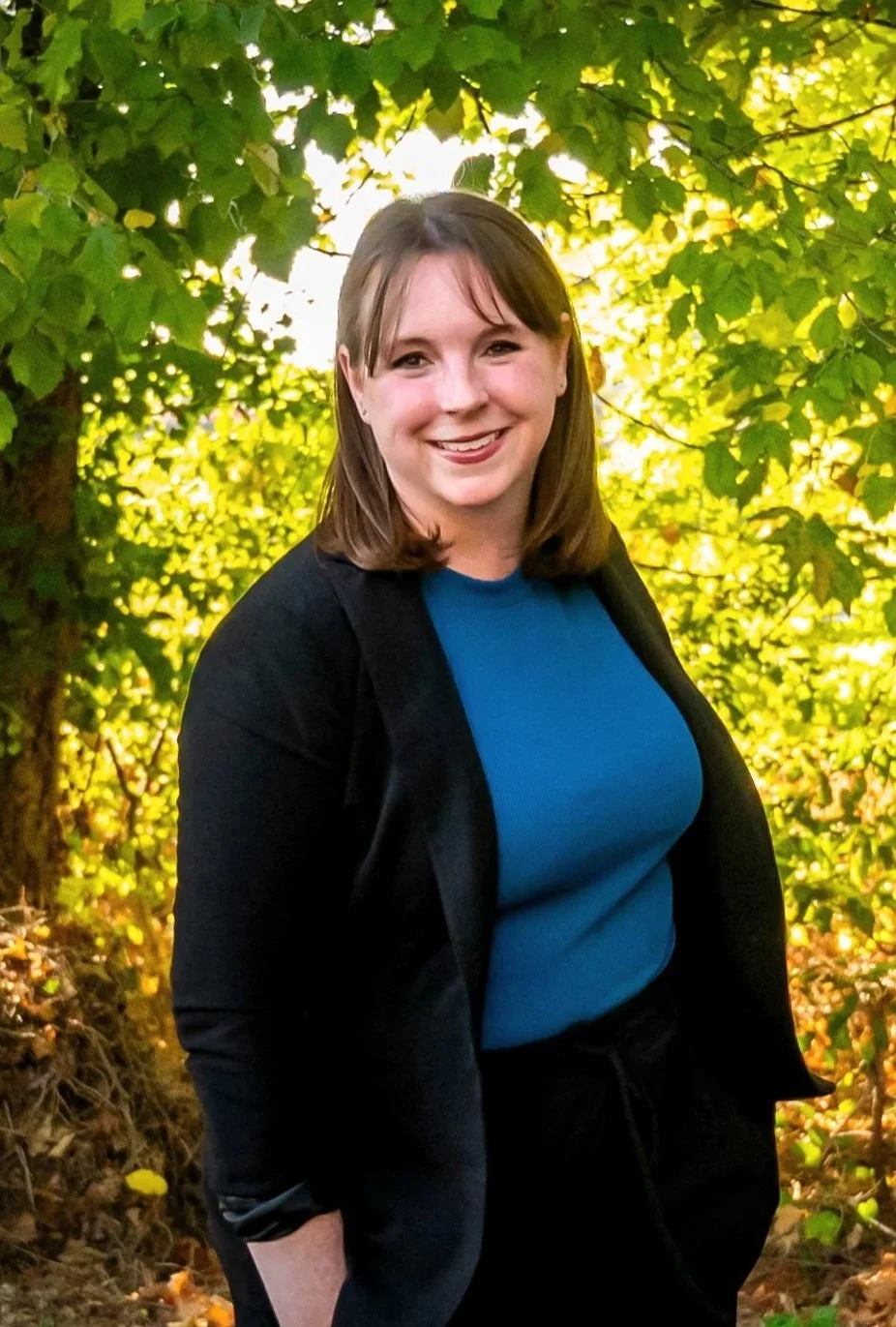 Woman smiling in a natural setting with green foliage background.
