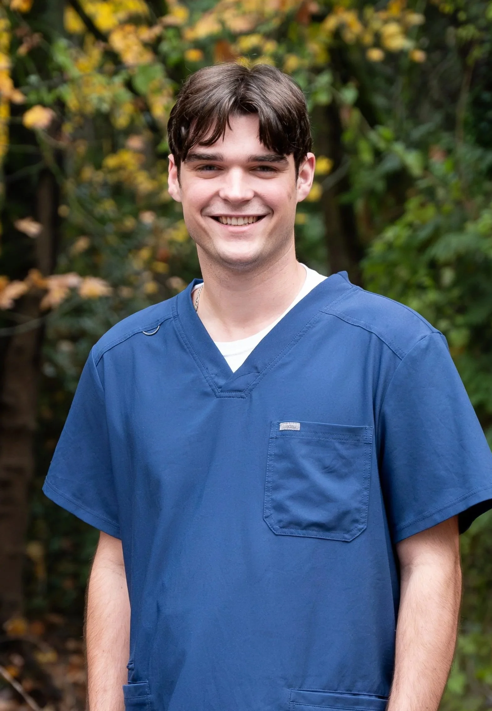 Man standing with tree in the background wearing black scrubs
