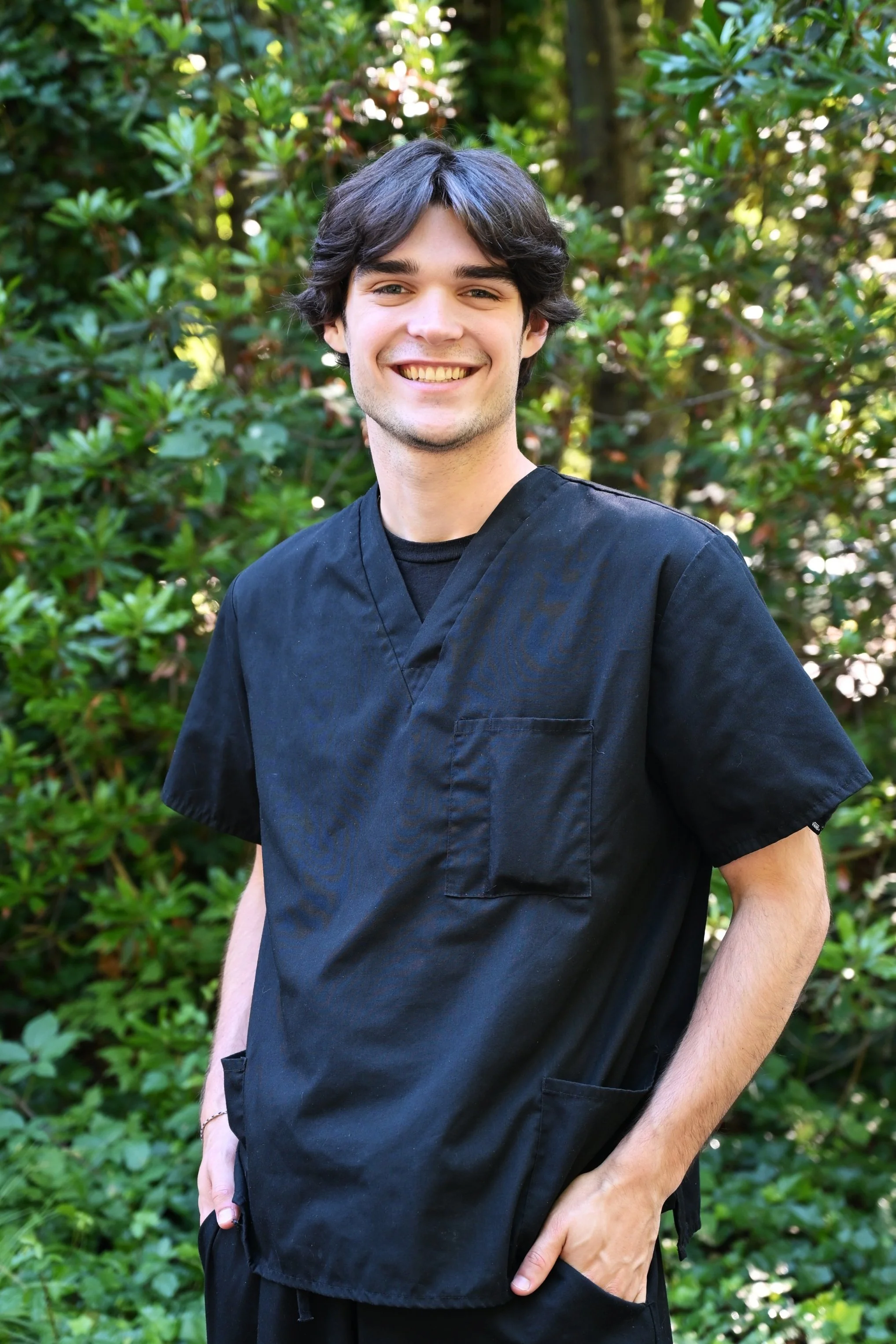 Man standing with tree in the background wearing black scrubs