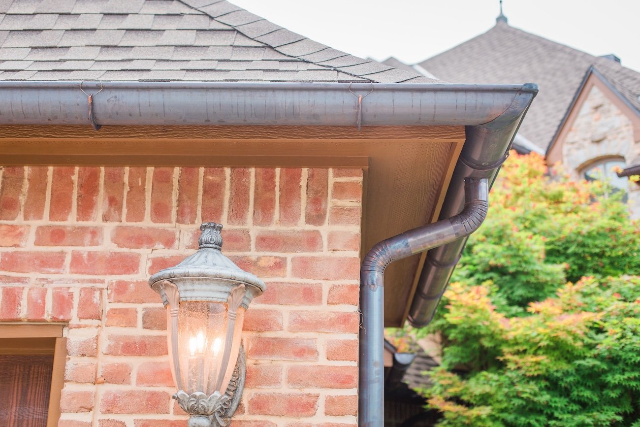Close-up of a brick house exterior with a vintage lantern, gutter, and downspout system.