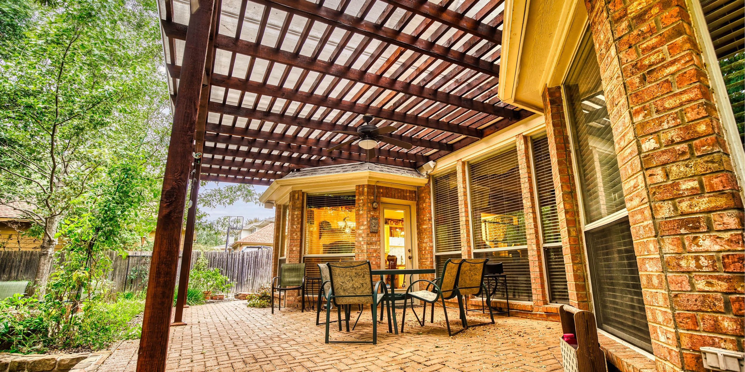 Covered patio with brick exterior, outdoor furniture, and ceiling fan.