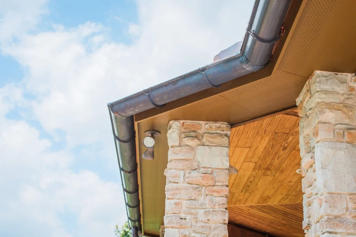 Stone pillar with a brown wooden roof and metal gutter against a blue sky.