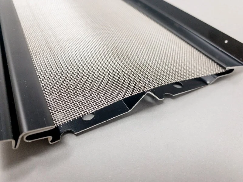Close-up of a metal mesh gutter guard with mounting edges on a gray background.