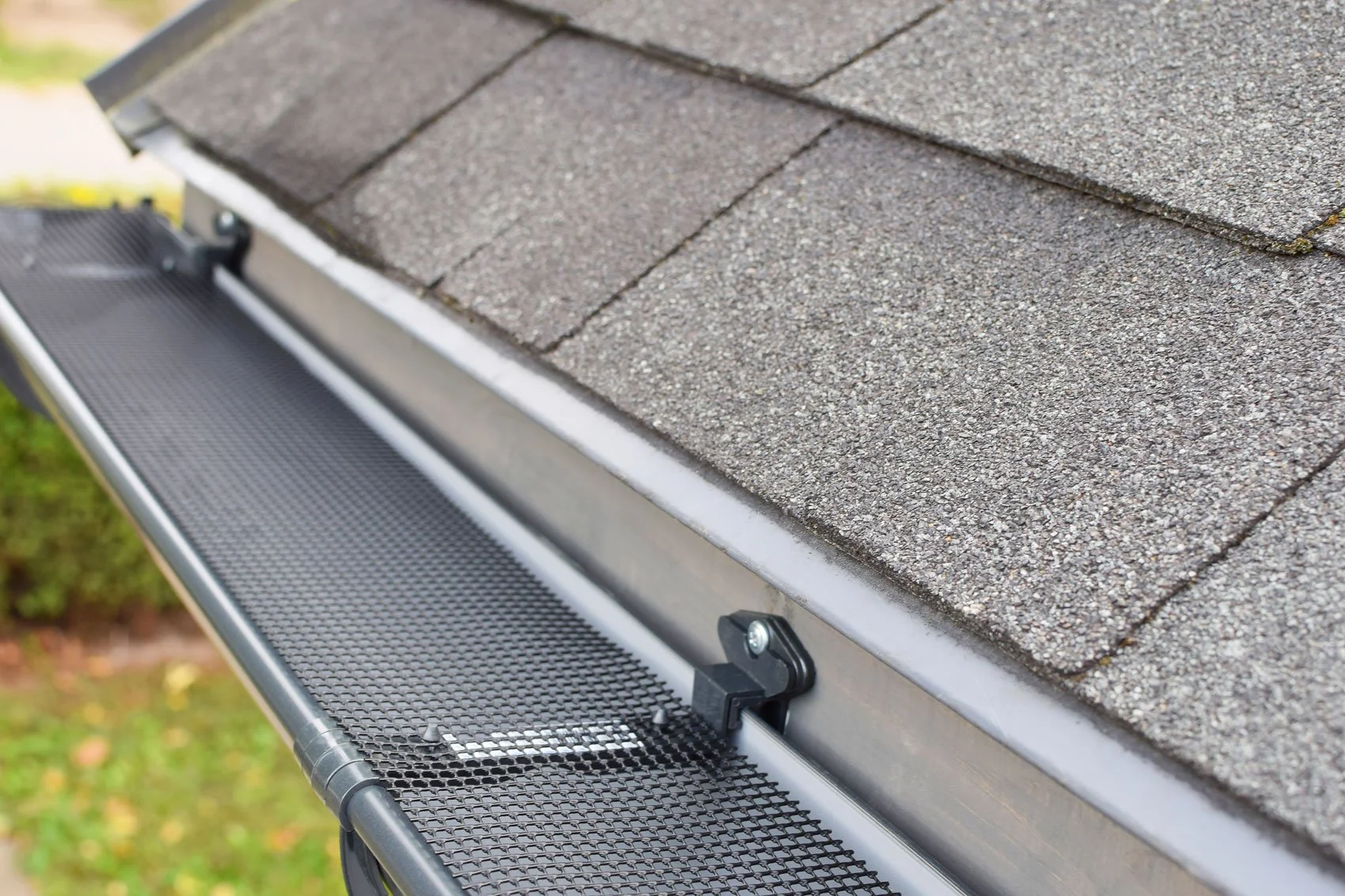 A roof with gray asphalt shingles and a metal gutter guard, designed to prevent debris from clogging the gutter.