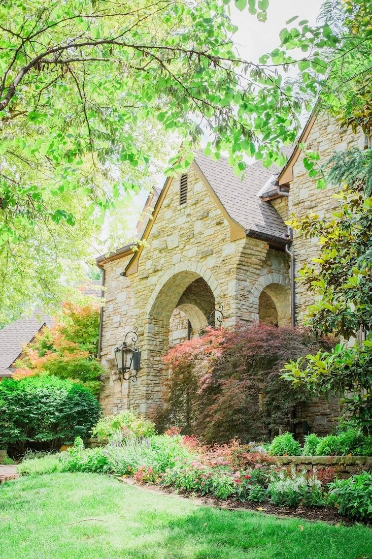 Stone house exterior with arched entry and lush garden landscaping.