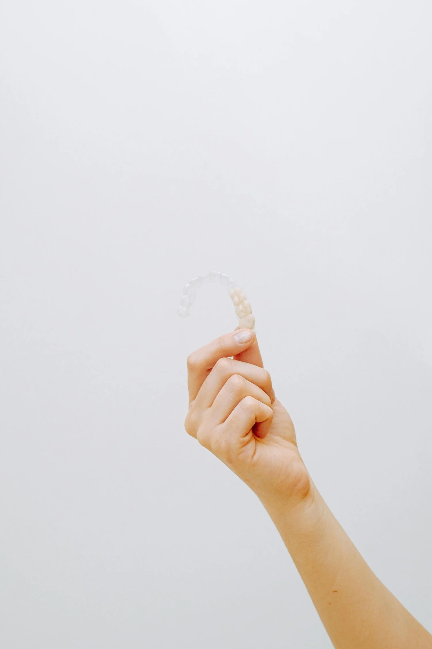 Hand holding a clear dental retainer against a plain white background.