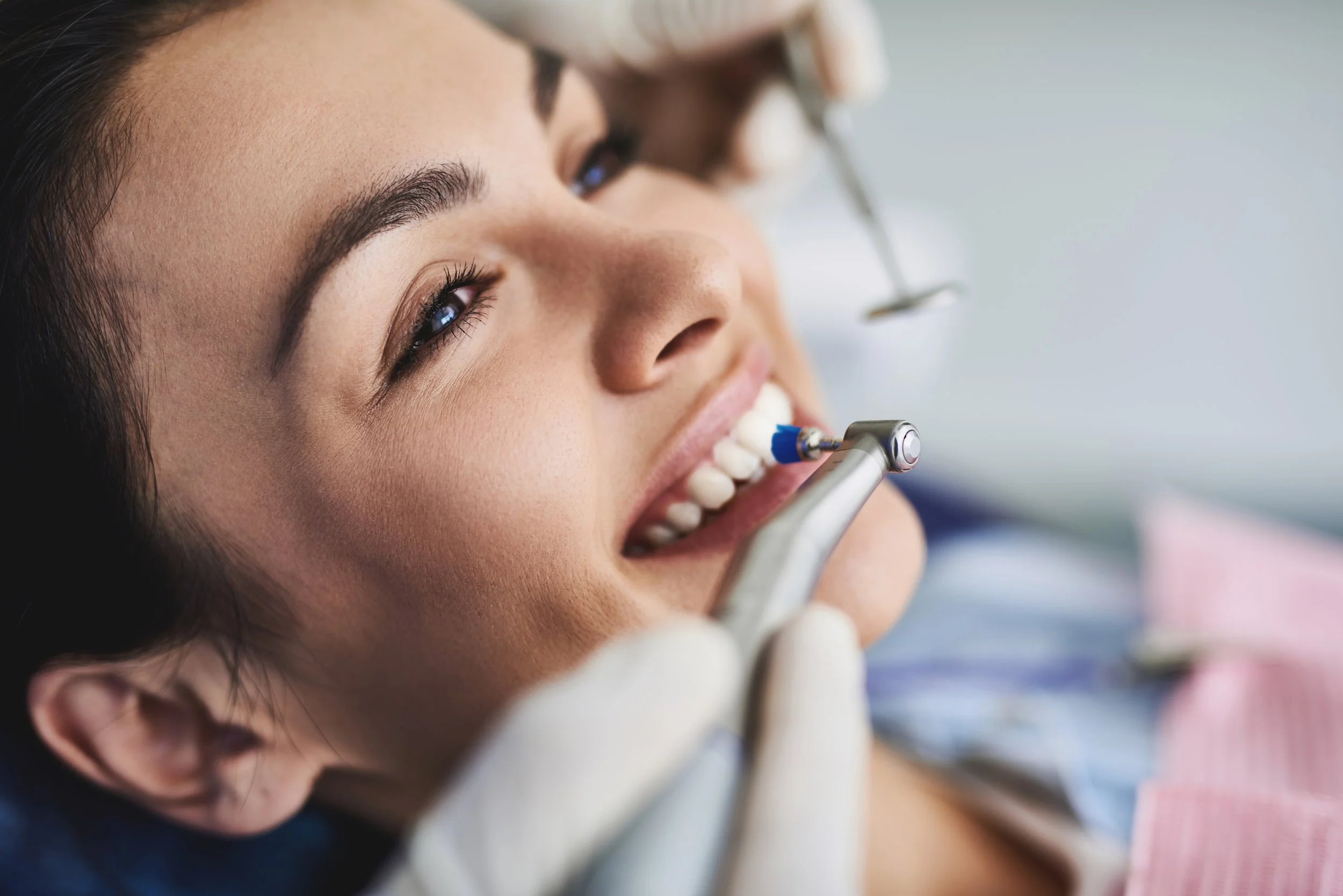 A woman lying back during a dental examination, with a dentist using dental tools near her mouth.