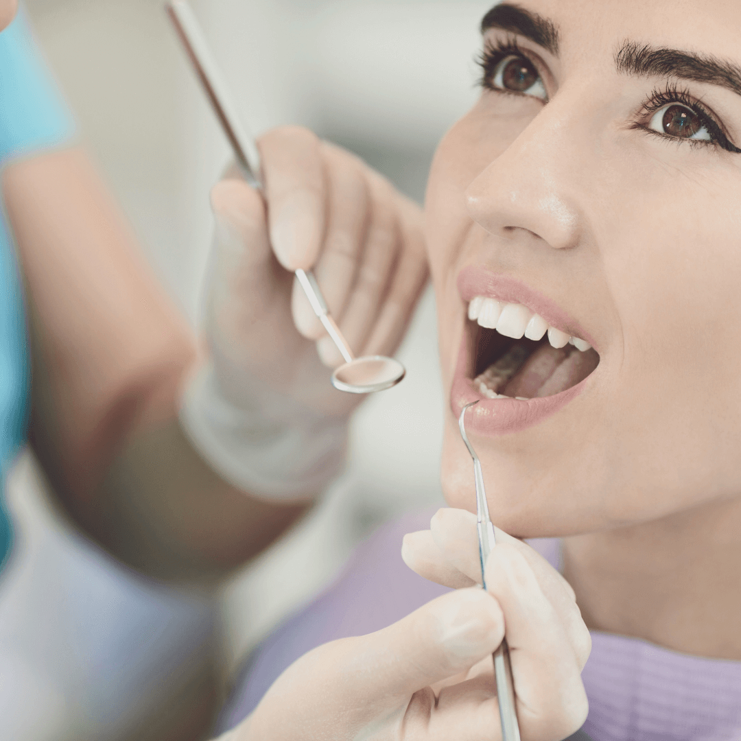 A woman at the dentist's office getting a dental check-up, with a dentist examining her mouth with dental tools.