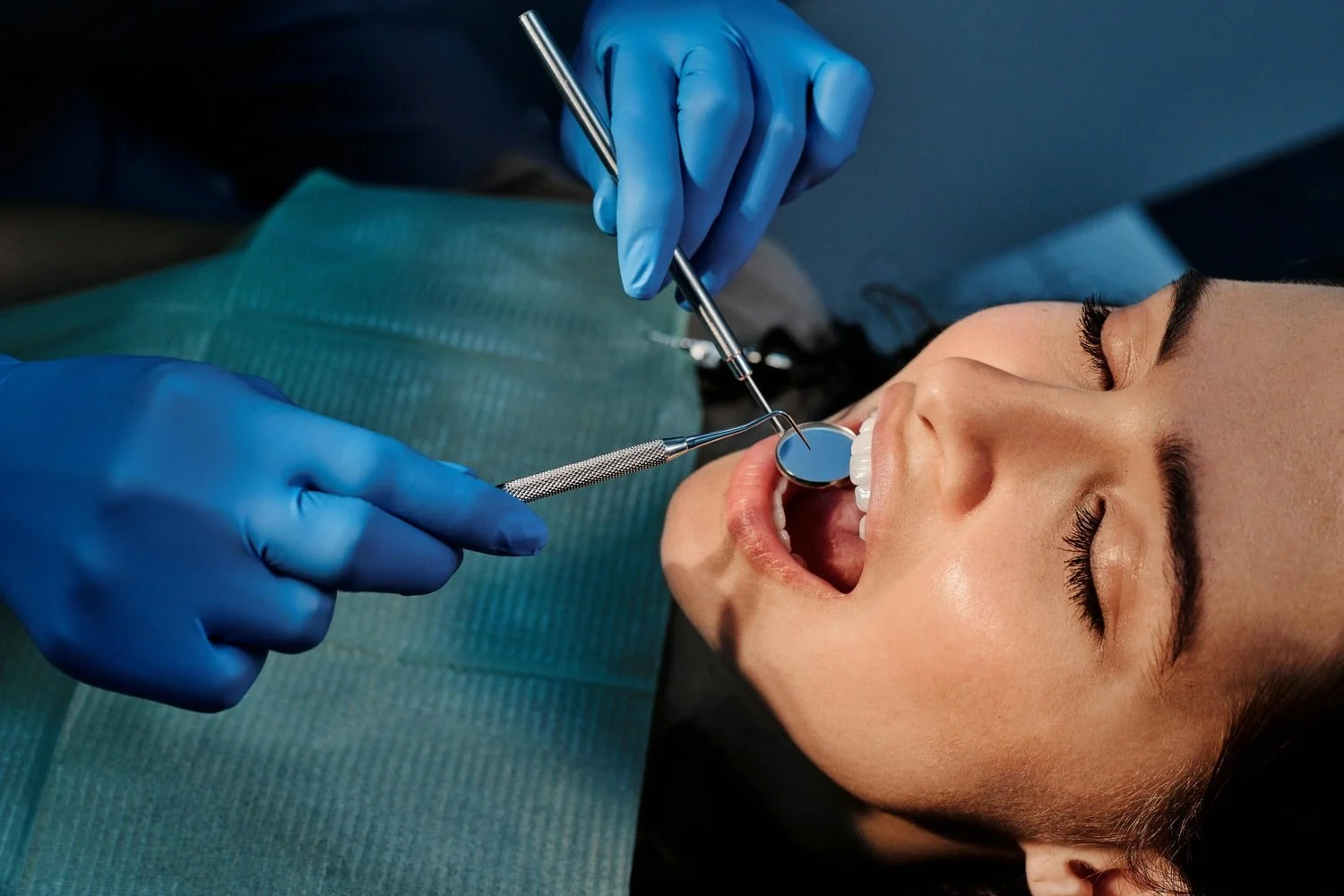 Dentist performing dental procedure on a patient with open mouth, using dental mirror and tools, in a dental clinic.