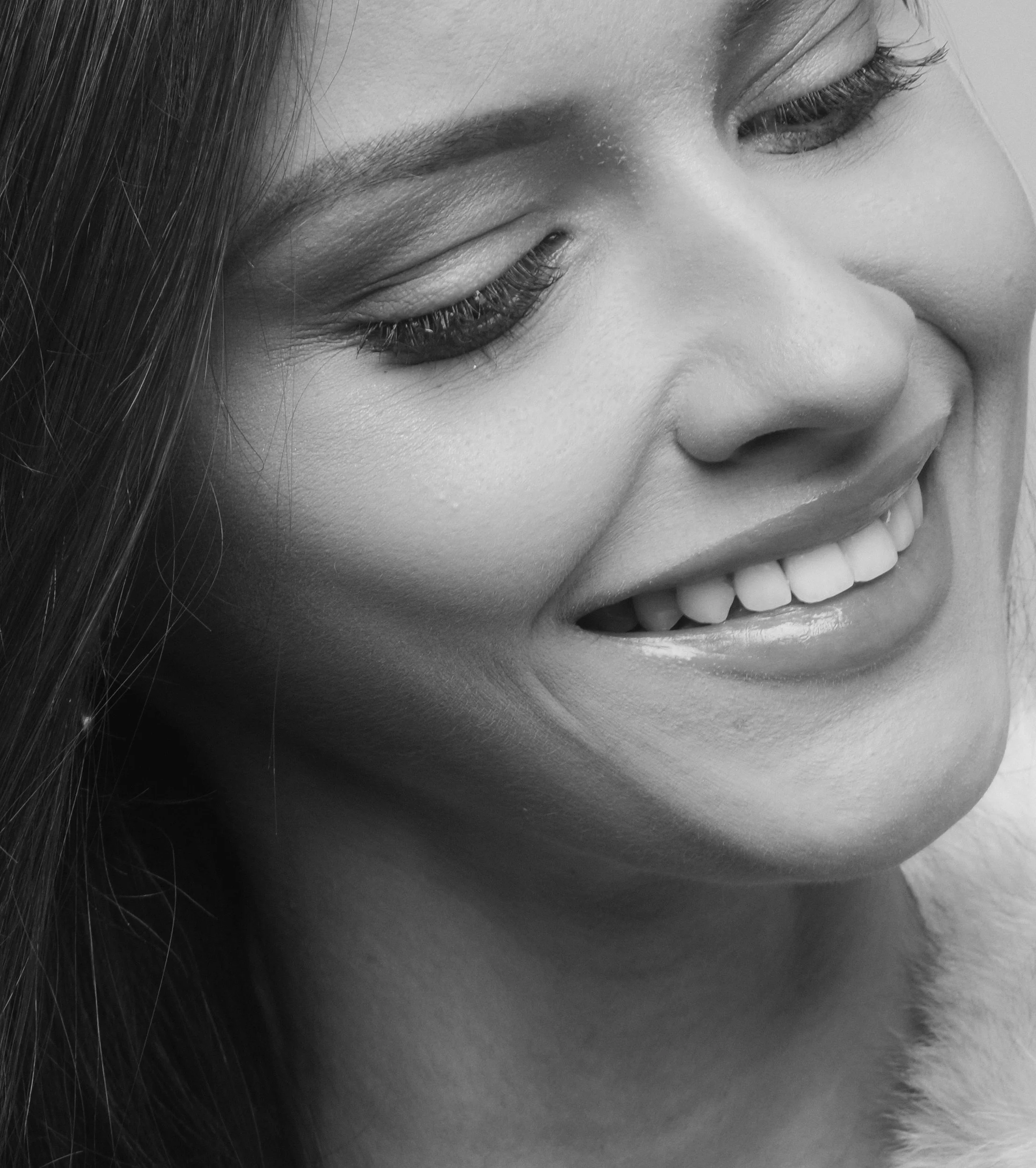 Close-up of a woman's smiling face with eyes closed, showing teeth, in black and white