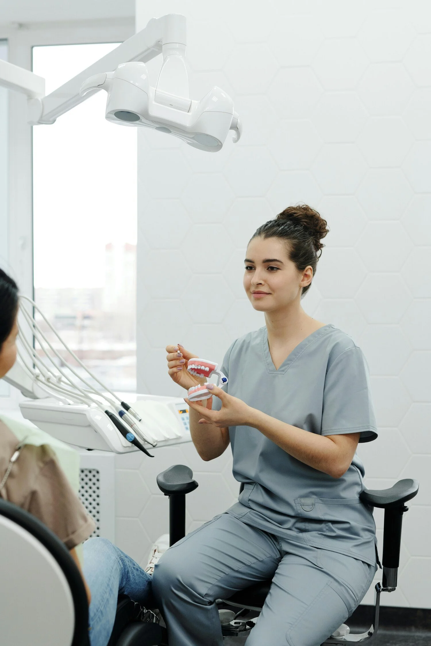 A female dentist holding a dental model and explaining dental care to a patient in a modern dental office.