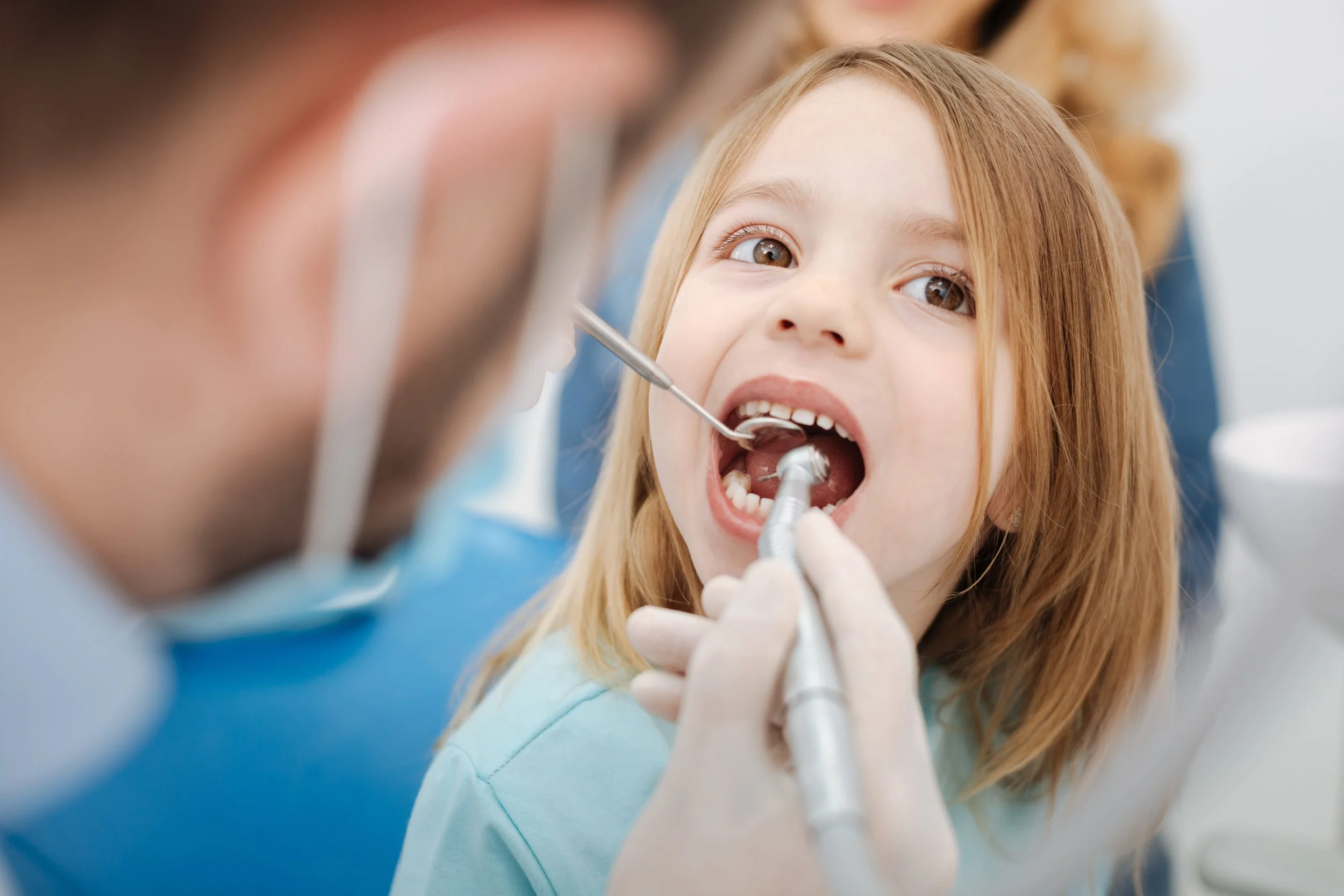 A young girl at the dentist's office with her mouth open while a dentist examines her teeth.