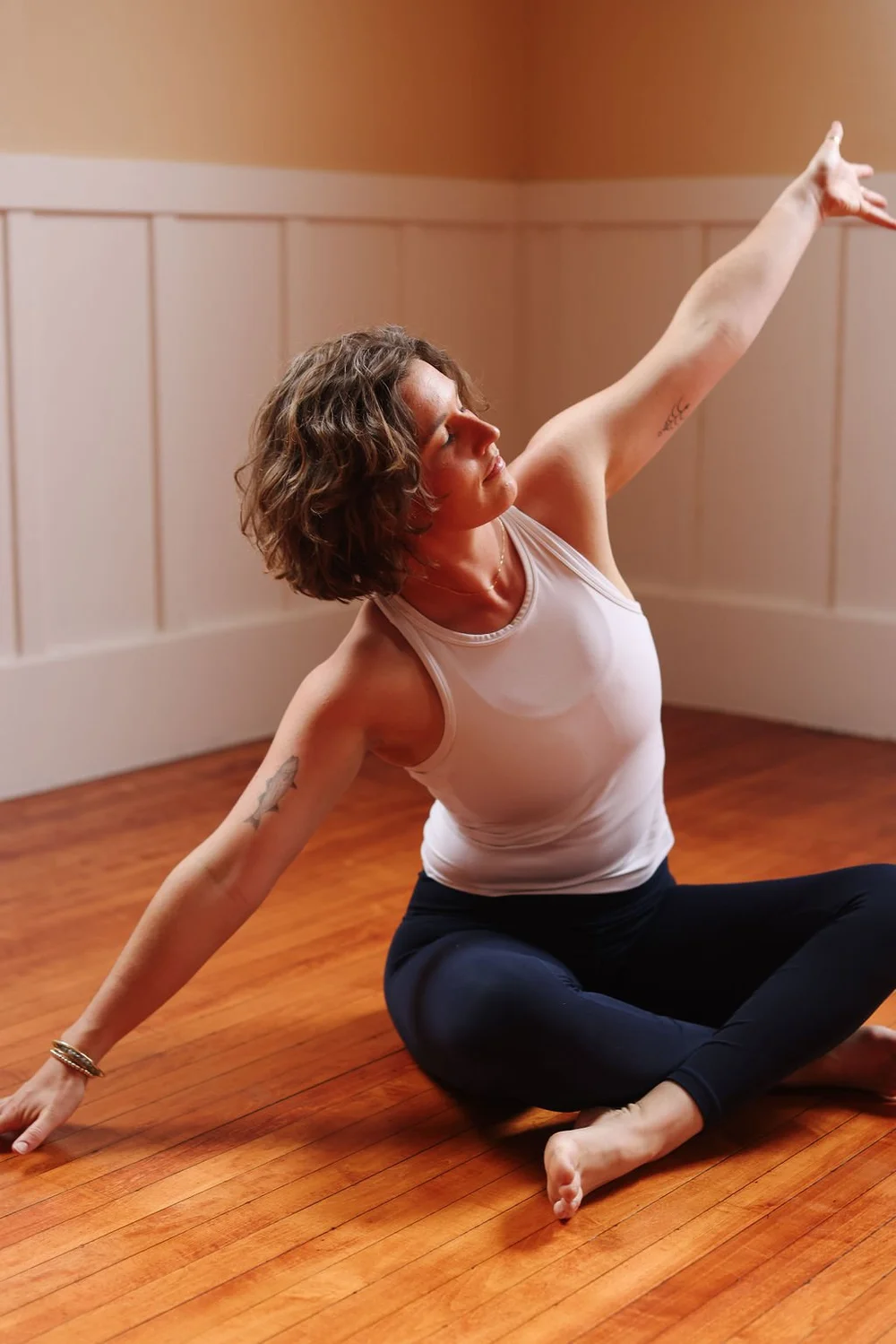 Haley Havelock in a seated twist, reaching up in a sunlit studio