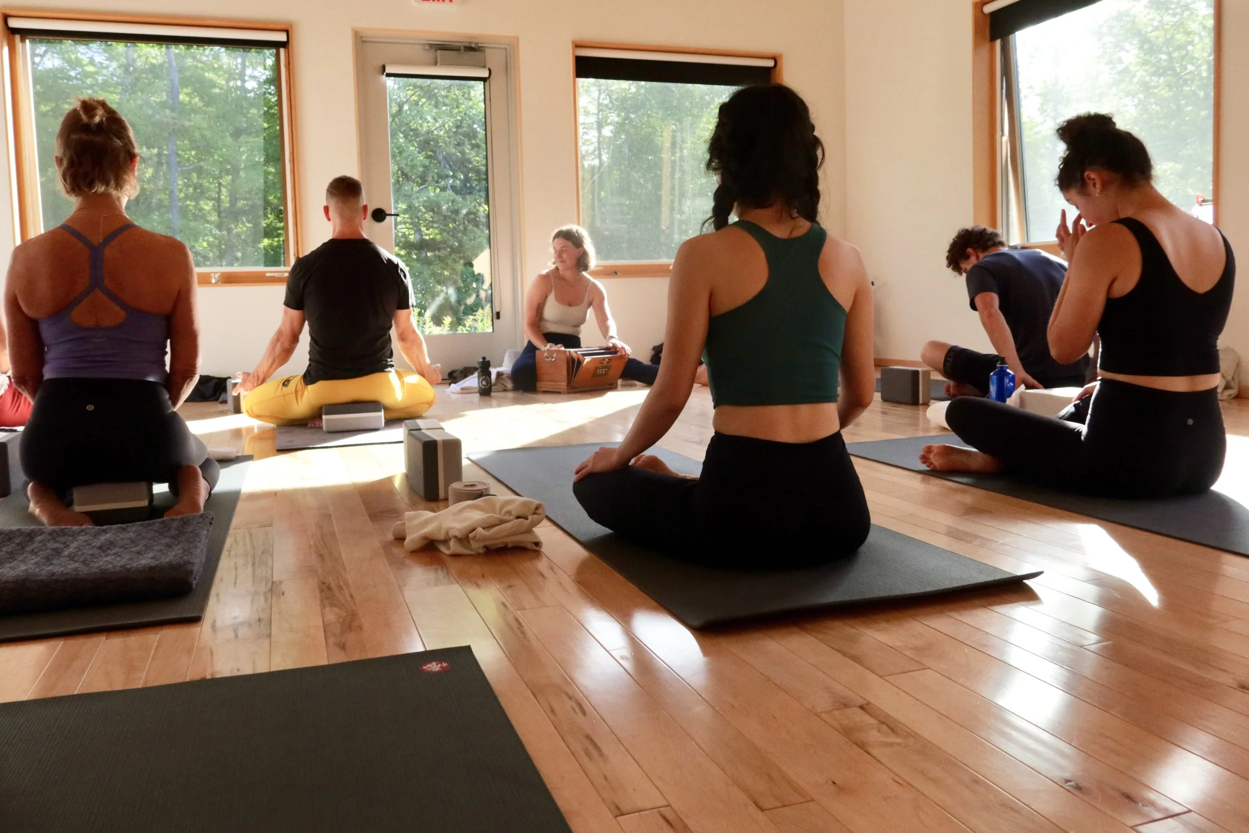 A group yoga class seated on mats in a sunlit studio