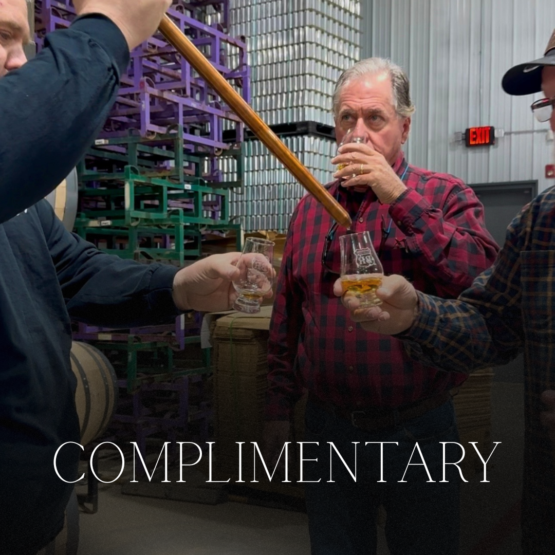 Three men in a distillery, with one man holding a glass of whiskey and another pouring whiskey into the glass.