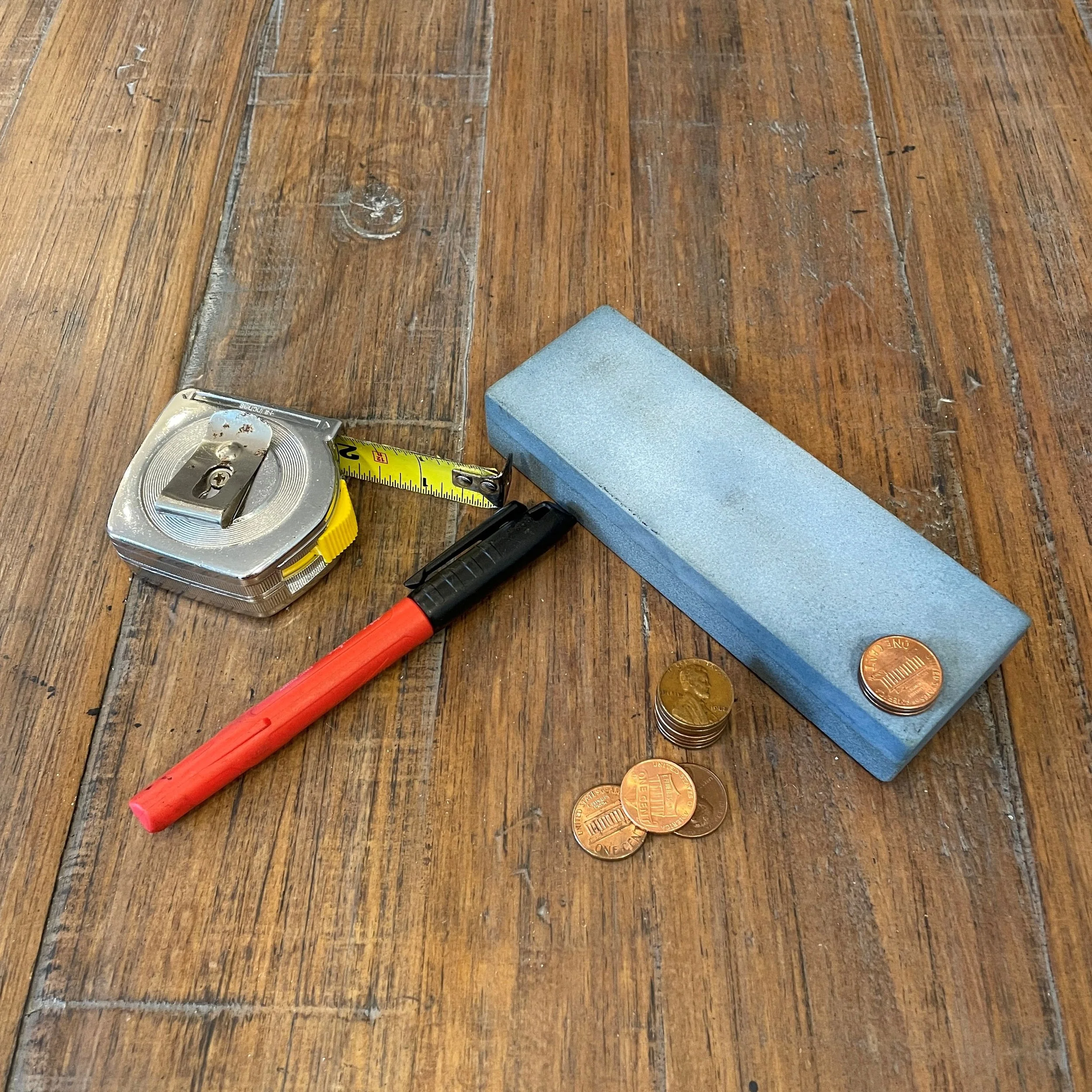 Items needed to determine a most recent sharpening angle or sharpen to a specific angle using a coin stack for reference.  Items include a ruler, a sharpening stone, a permanent marker and several pennies.