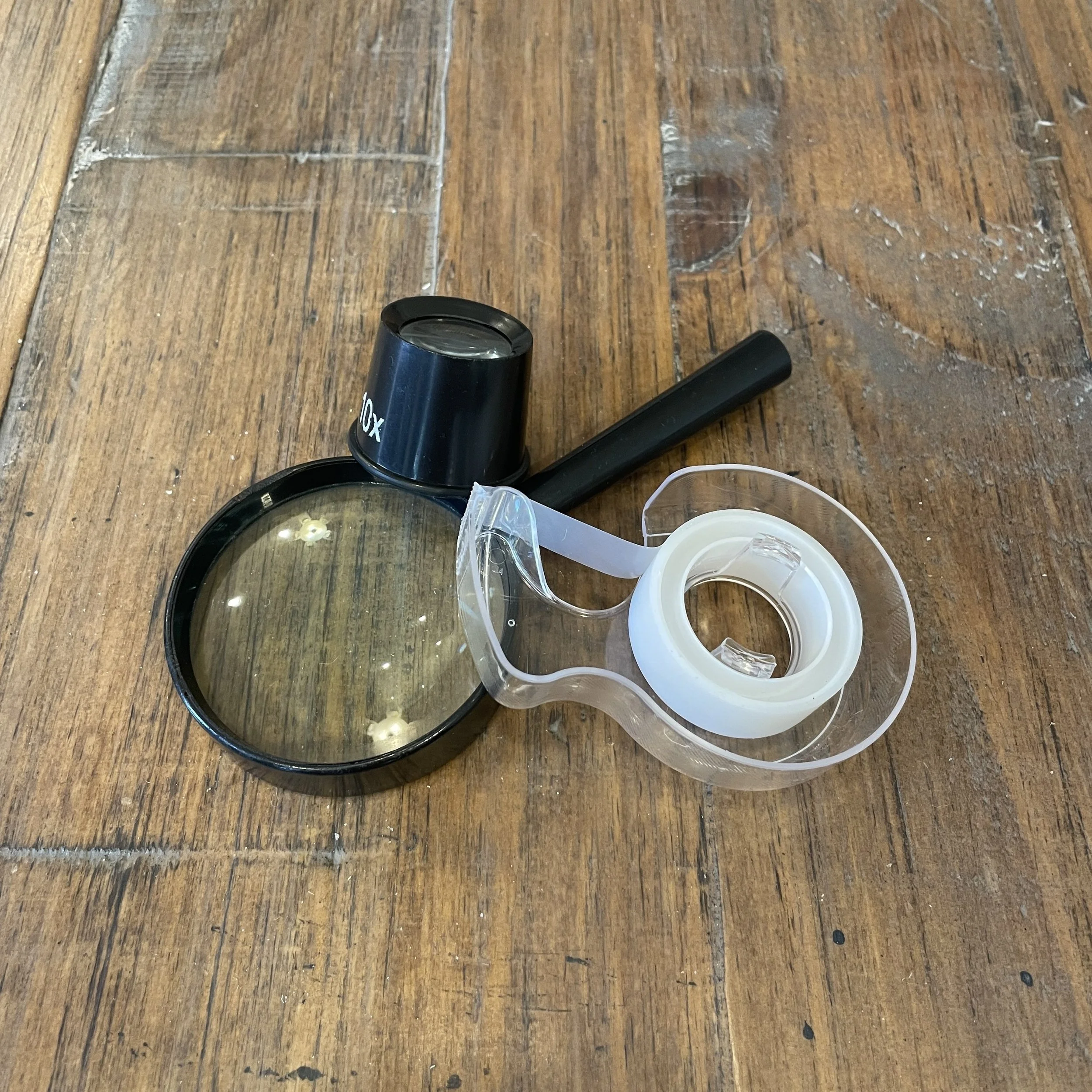 Optional items needed to sharpen a knife or cutting tool using a coin stack.  Items include transparent tape to secure the coin stack and a magnifying glass or jewelers loupe to inspect the edge for signs of edge rolling, denting or chipping.