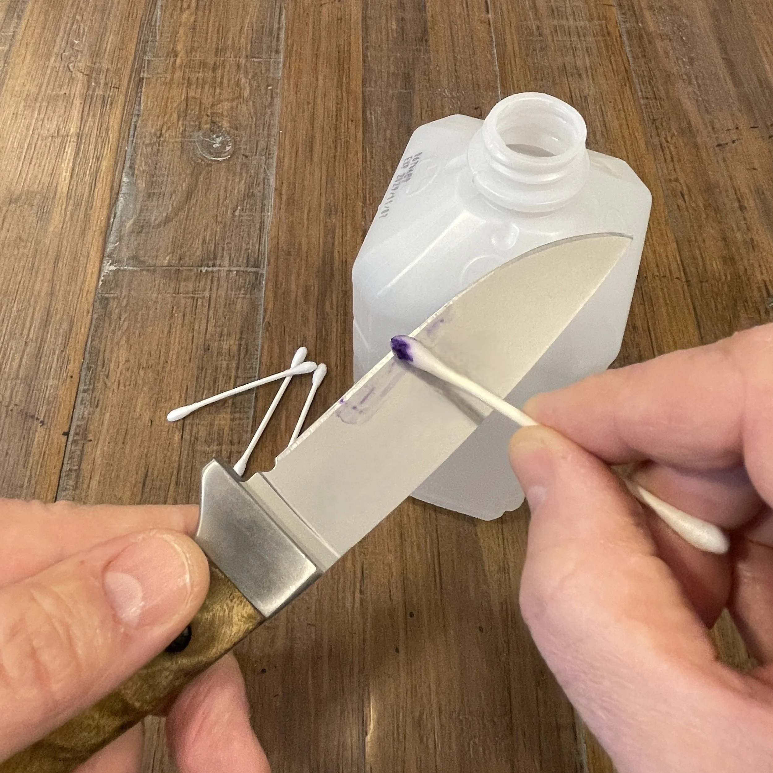 Removing permanent marker from a knife blade with rubbing alcohol and a cotton swab after determining the most recent sharpening angle using a coin stack for reference.