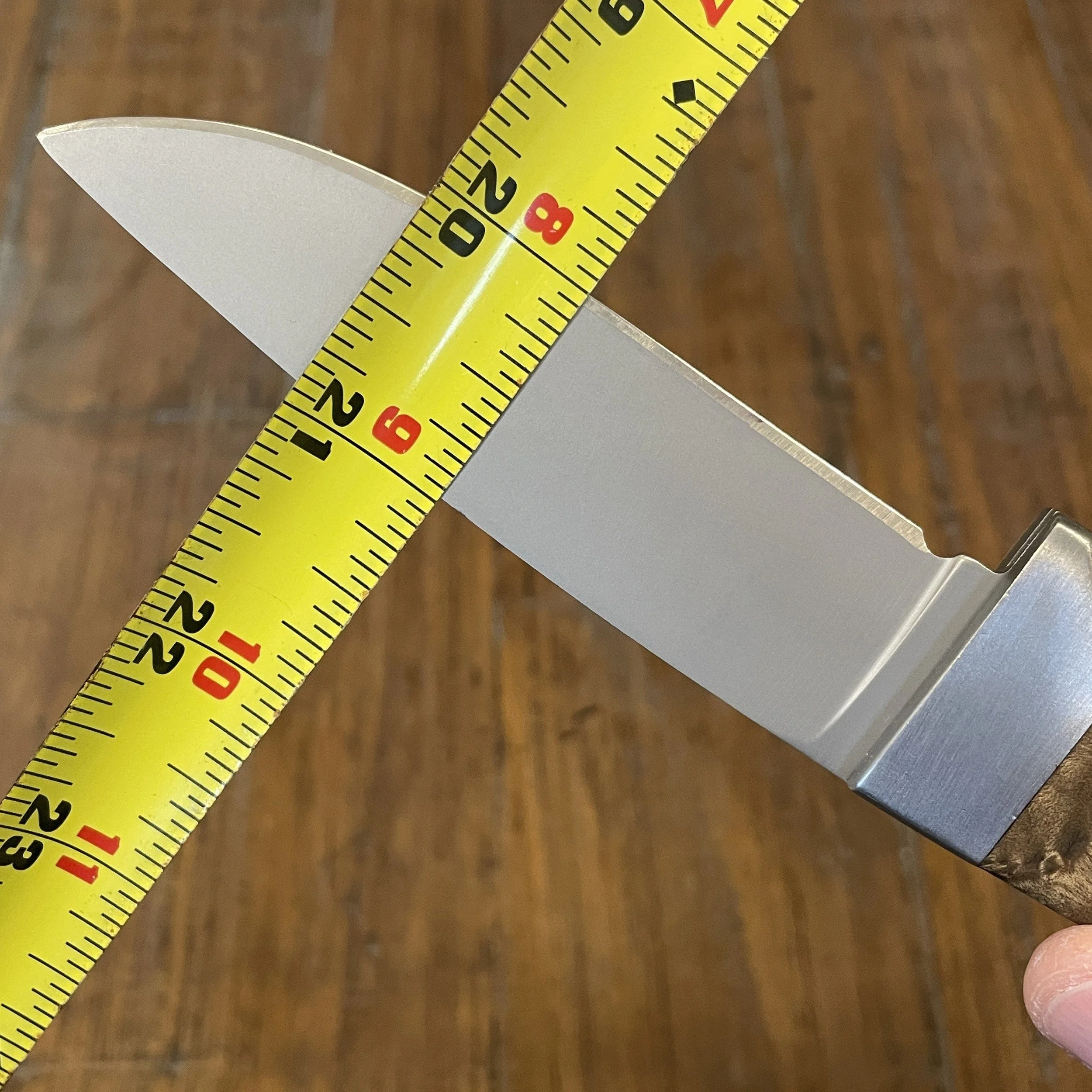 A tape measure laid across a knife blade measuring the height of the blade from the spine to cutting edge in preparation for sharpening the blade to a desired angle using a coin stack for reference.