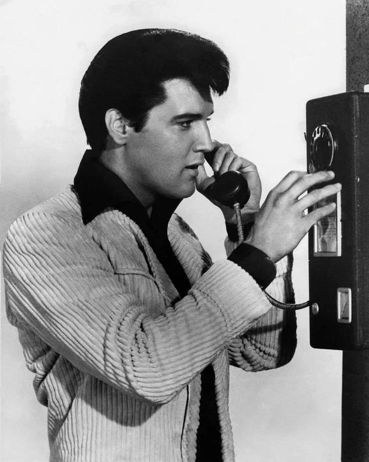 Elvis is talking on a payphone.