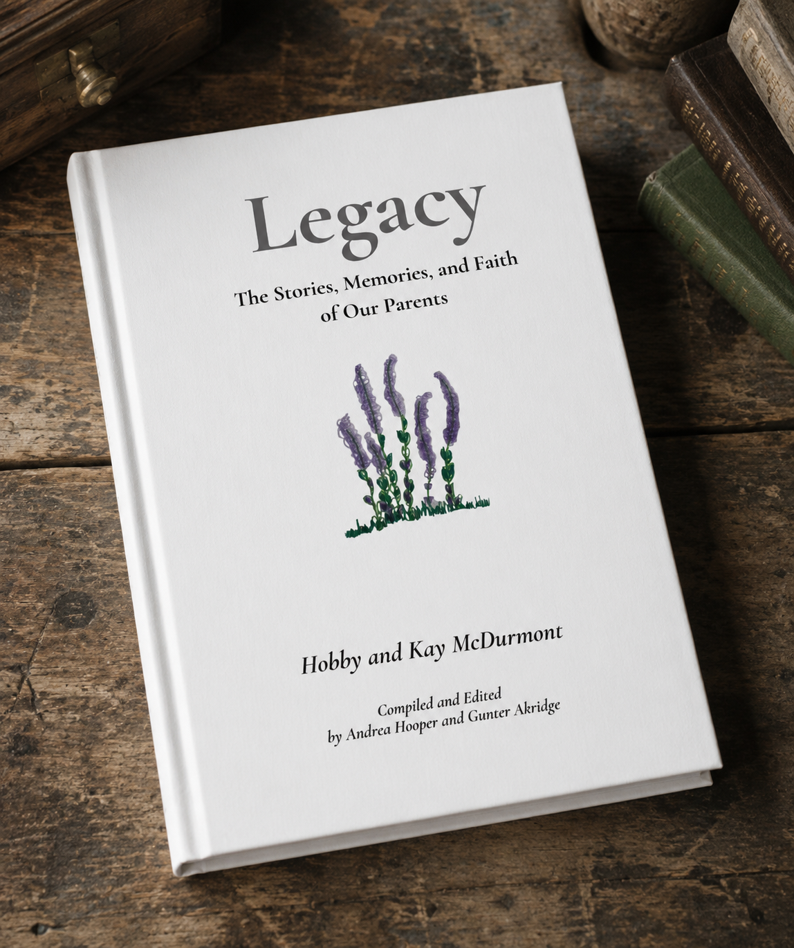 White hardcover book titled 'Legacy: The Stories, Memories, and Faith of Our Parents' with a lavender illustration on the cover, placed on a rustic wooden surface alongside other books.