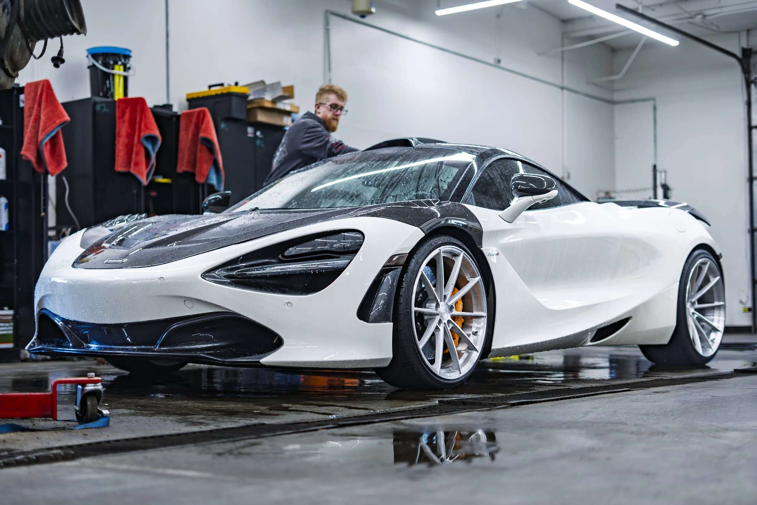 A man washing a white and black sports car inside a garage