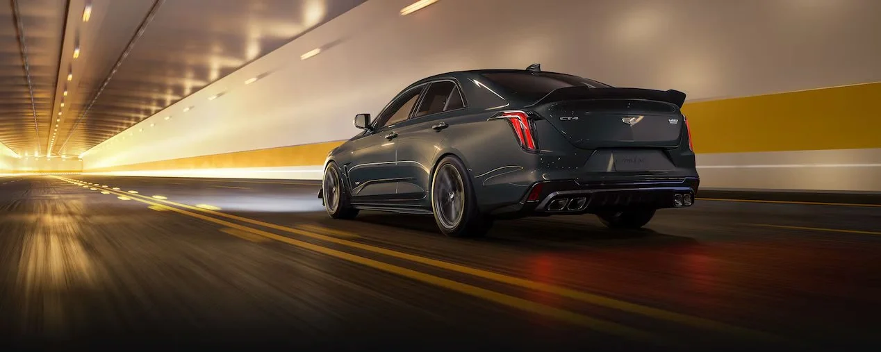 A black luxury sedan driving through a tunnel at night with motion blur and yellow walls.