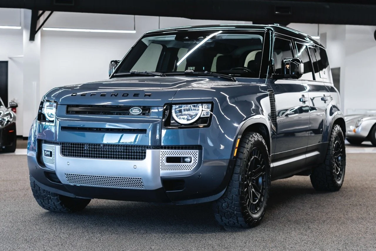 A dark blue Land Rover Defender SUV parked indoors, with a modern interior and other vehicles visible in the background.