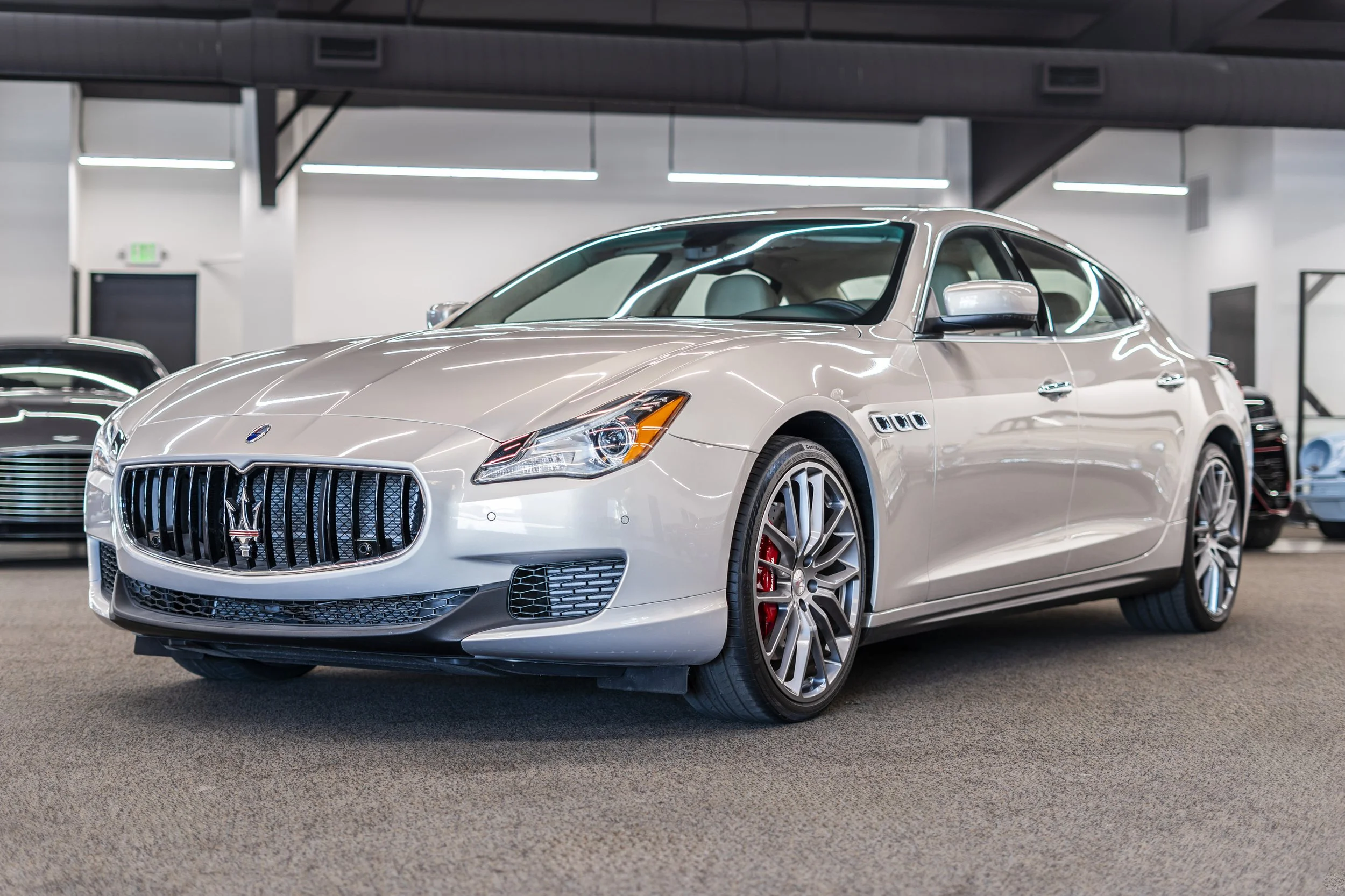 A beige luxury car with a prominent front grille and sporty wheels parked in an indoor car showroom.
