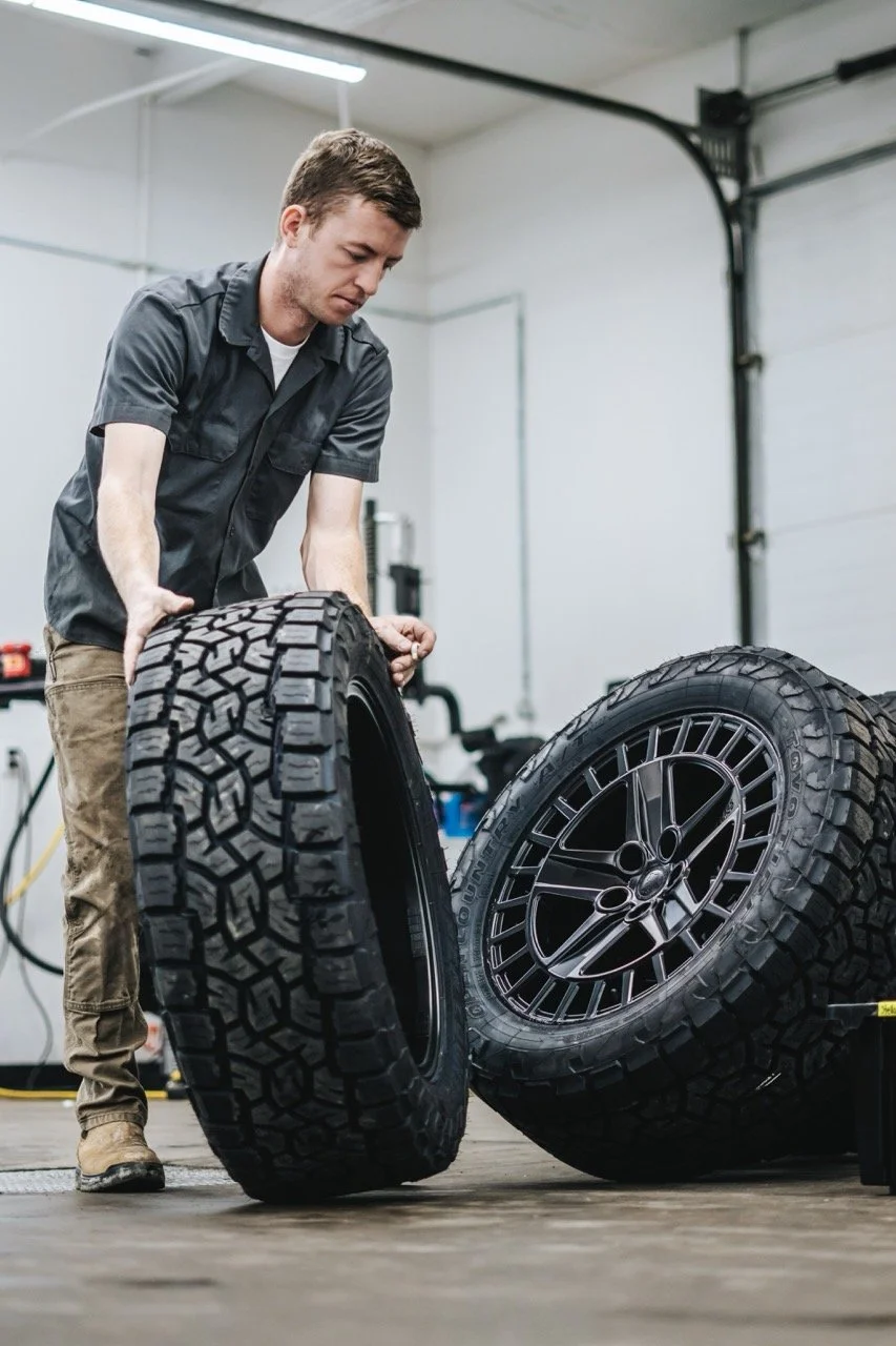A man is inspecting or working on a large off-road tire inside a garage or workshop.