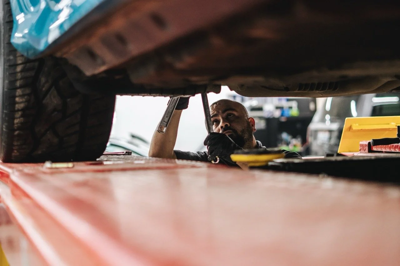 Mechanic working underneath a car in a garage, inspecting or repairing the vehicle.
