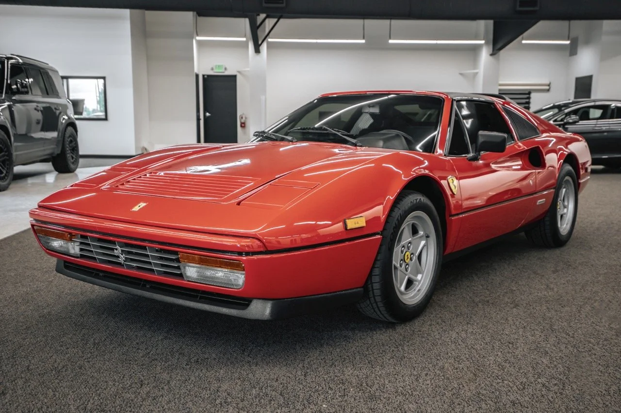 Red Ferrari sports car inside a showroom, with other vehicles in the background.
