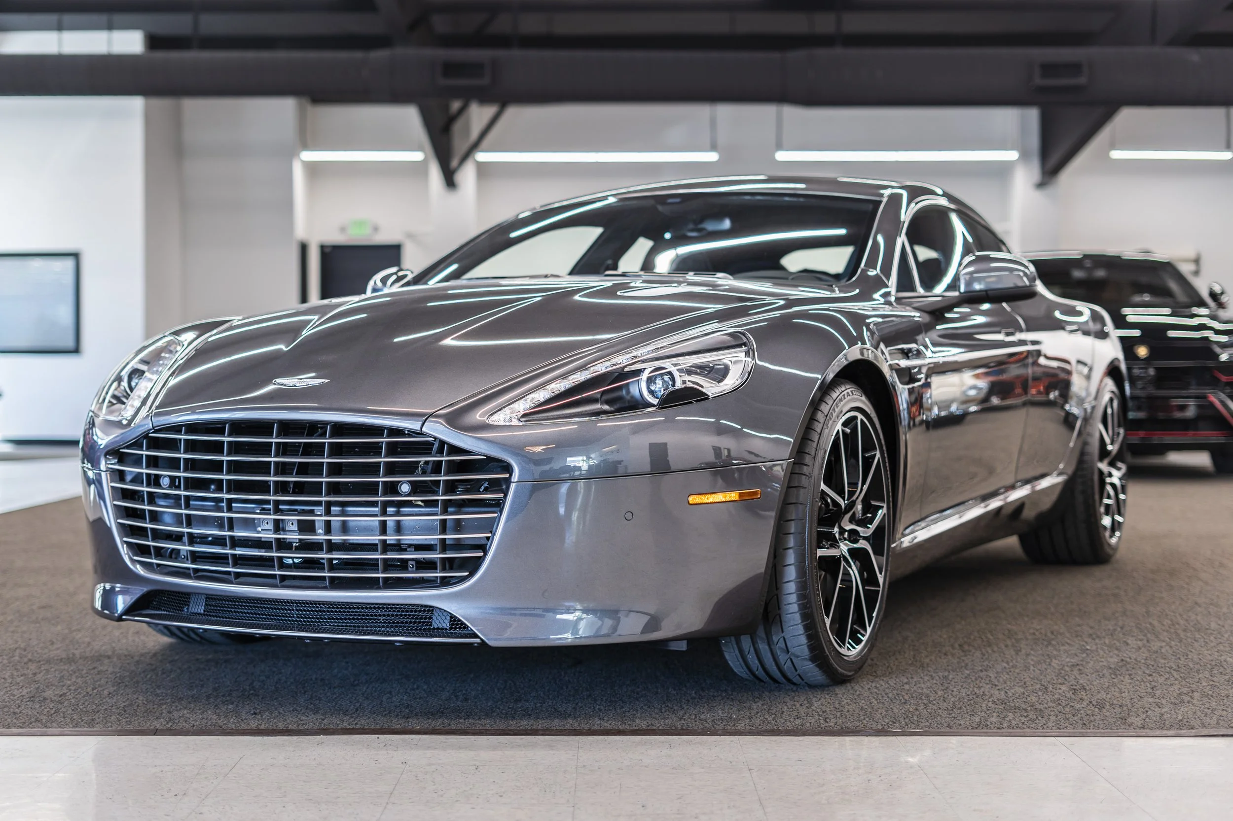 A silver luxury sports car with a sleek design, parked indoors on a showroom floor.