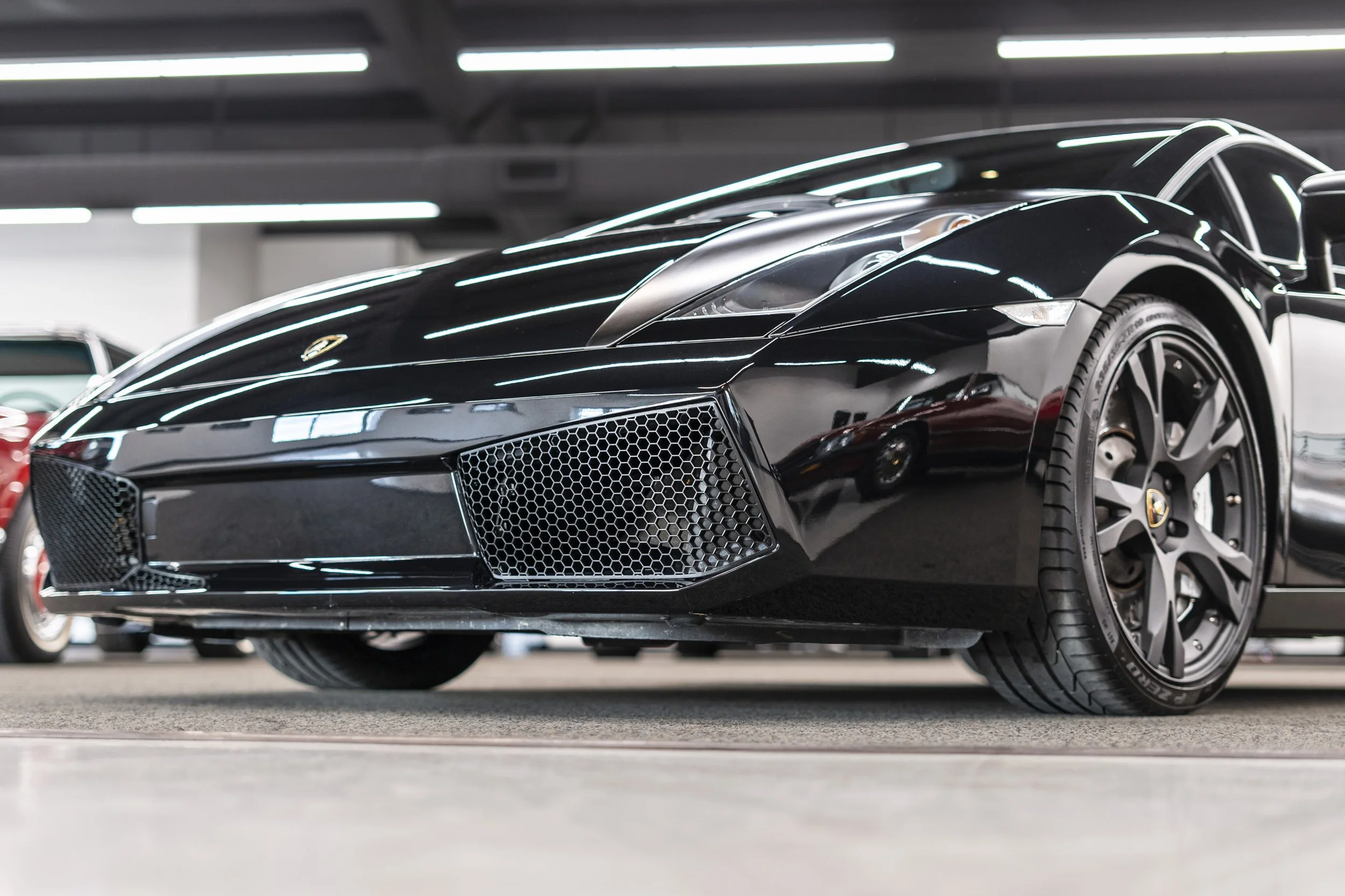 Black Lamborghini sports car parked indoors, reflecting ceiling lights, with a sleek design and low profile.