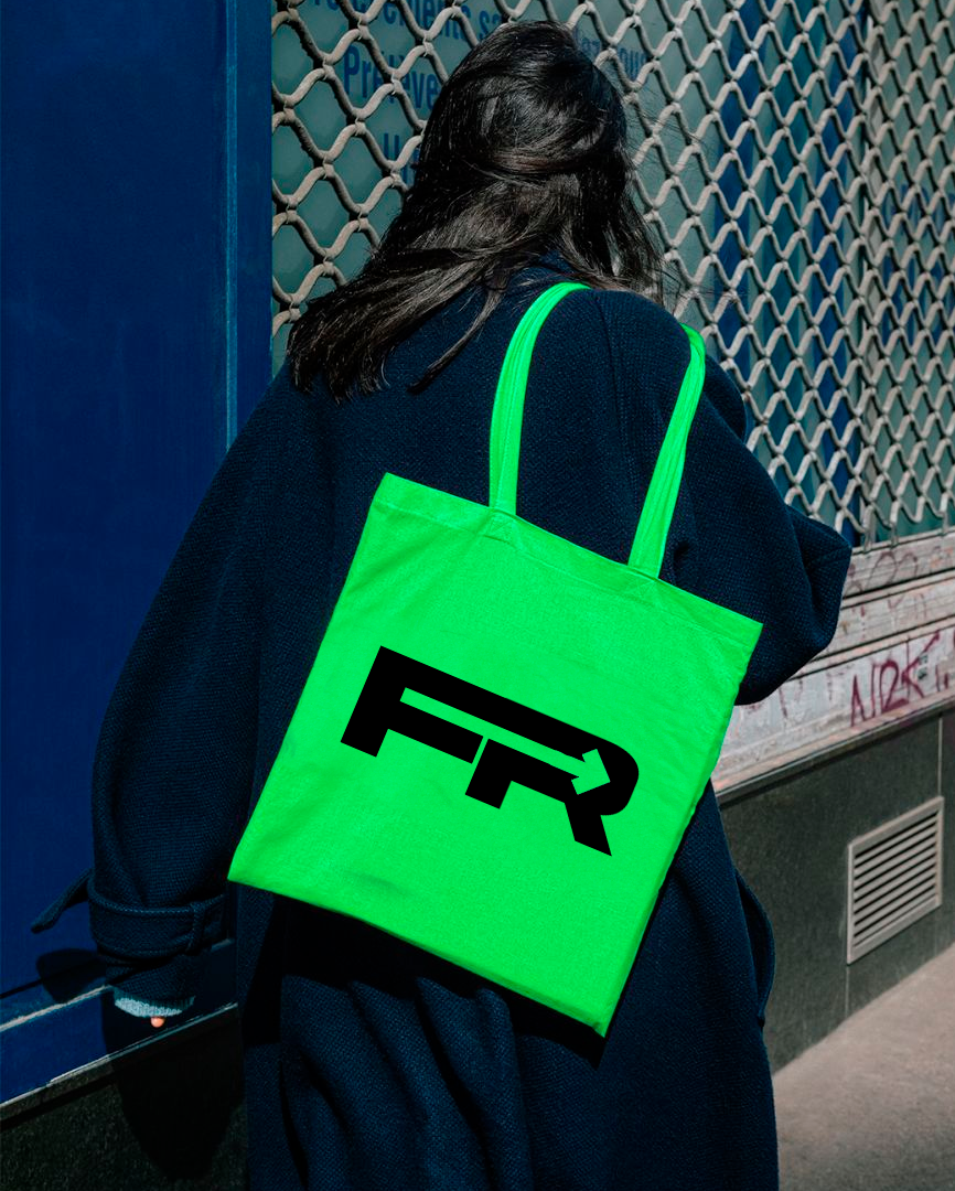Persona con bolso verde de tela y logo en negro, de espaldas, en una calle
