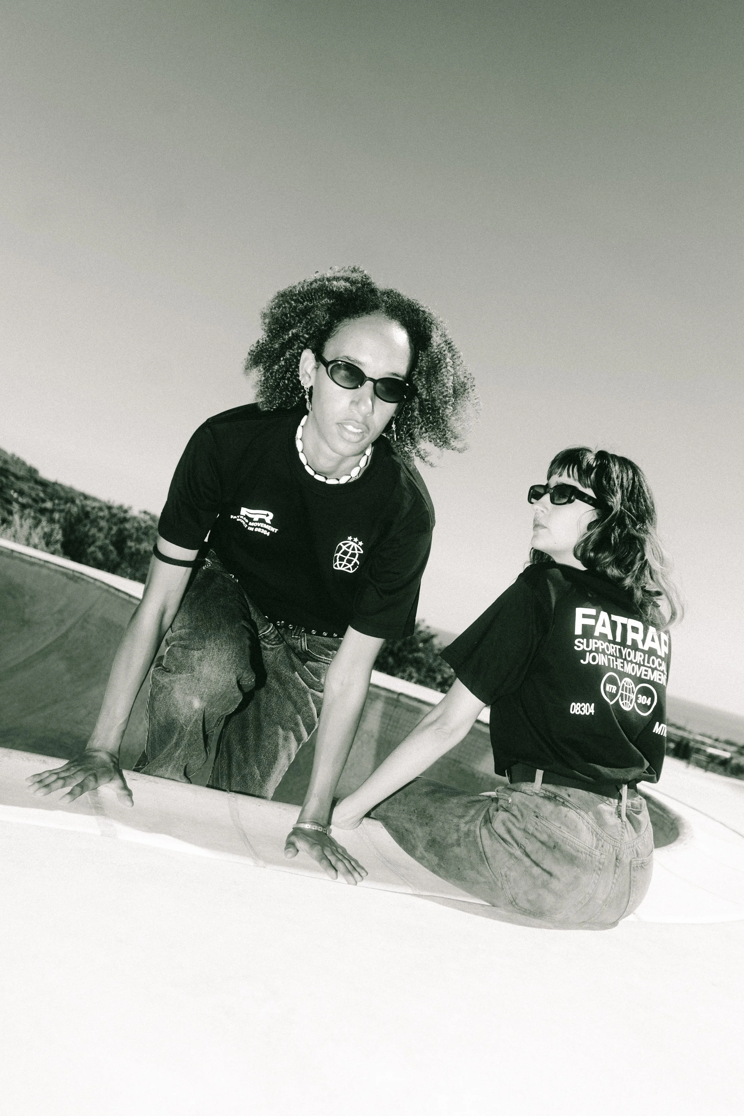 Dos mujeres con gafas oscuras posando en un parque de patinaje en un día soleado