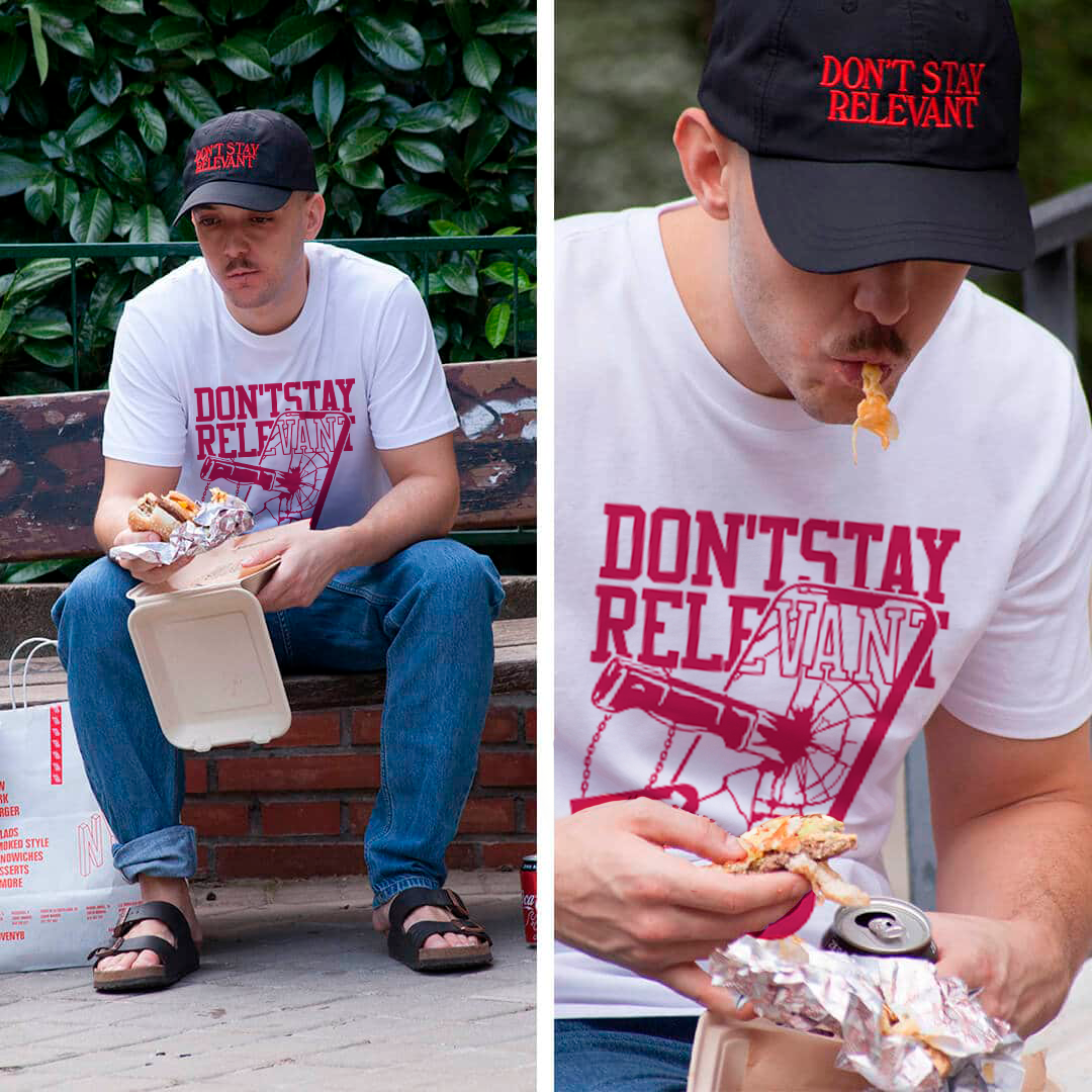 Joven sentado en un banco comiendo un sándwich, viste una camiseta blanca con letras rosas y una gorra negra con letras rojas que dicen "DON'T STAY RELEVANT". En la segunda imagen, el mismo joven sigue comiendo el sándwich y una lata de refresco.