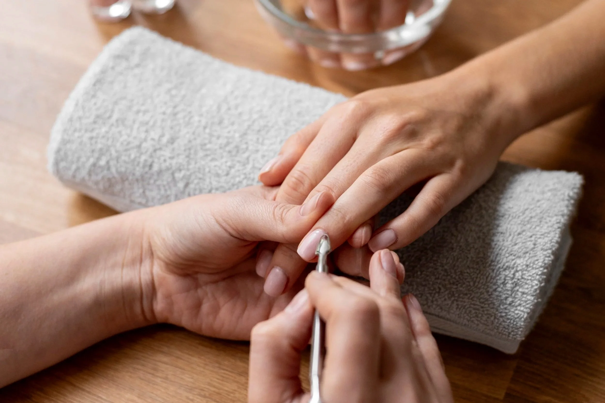 A person receiving a manicure, with another person using a small tool on their nails, while their hand rests on a towel.