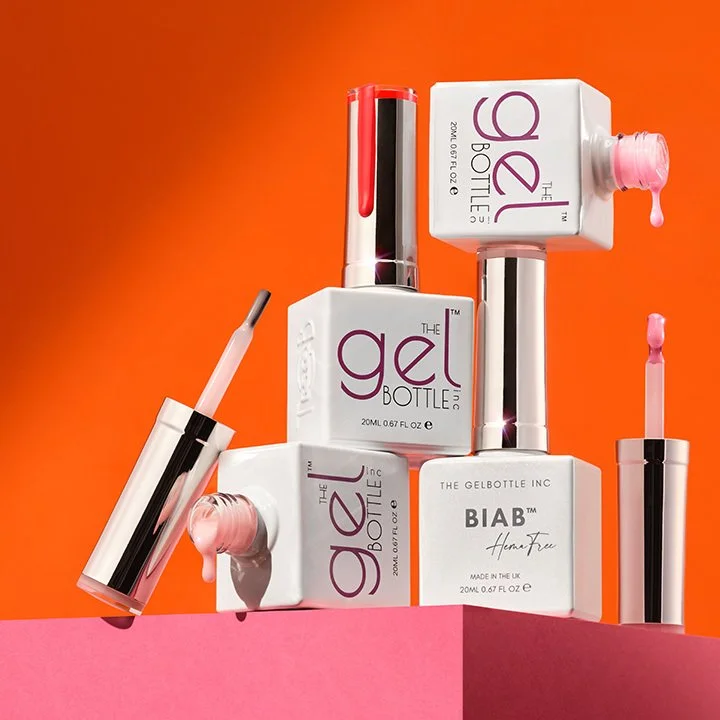 A display of colorful nail products, including gel polish bottles with applicators, arranged on a pink and orange background.